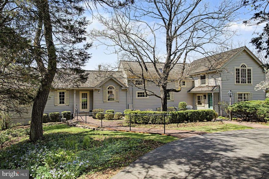 Tucked quietly along a winding drive in the heart of Tinicum Township, this enchanting Bucks County residence offers a rare blend of character, flexibility, and privacy on a beautifully landscaped setting. A series of thoughtfully connected living spaces creates a uniquely versatile floor plan, ideal for today’s evolving lifestyles. Multiple entrances and distinct wings provide natural separation for guests, extended family, or work-from-home arrangements, while maintaining a cohesive and inviting flow throughout the home. Rich in architectural detail, the interiors showcase wide-plank wood floors, exposed beams, deep-set windows, and a striking stone fireplace anchoring one of several gathering spaces. Natural light pours into the home’s studio and living areas, enhancing its warm, artistic ambiance. The kitchen and baths are functional and full of charm, offering an excellent opportunity for future customization. Generous bedroom accommodations are thoughtfully distributed across the home, providing comfort and privacy.
Outdoors, mature trees, curated plantings, and meandering pathways create a peaceful, park-like setting. The property’s sense of seclusion is complemented by its proximity to the Delaware River, canal towpath, and the beloved villages and amenities of Upper Bucks County. A truly special offering—equally suited as a full-time residence, weekend retreat, or multi-generational living opportunity—this is a property that invites both quiet enjoyment and inspired living.