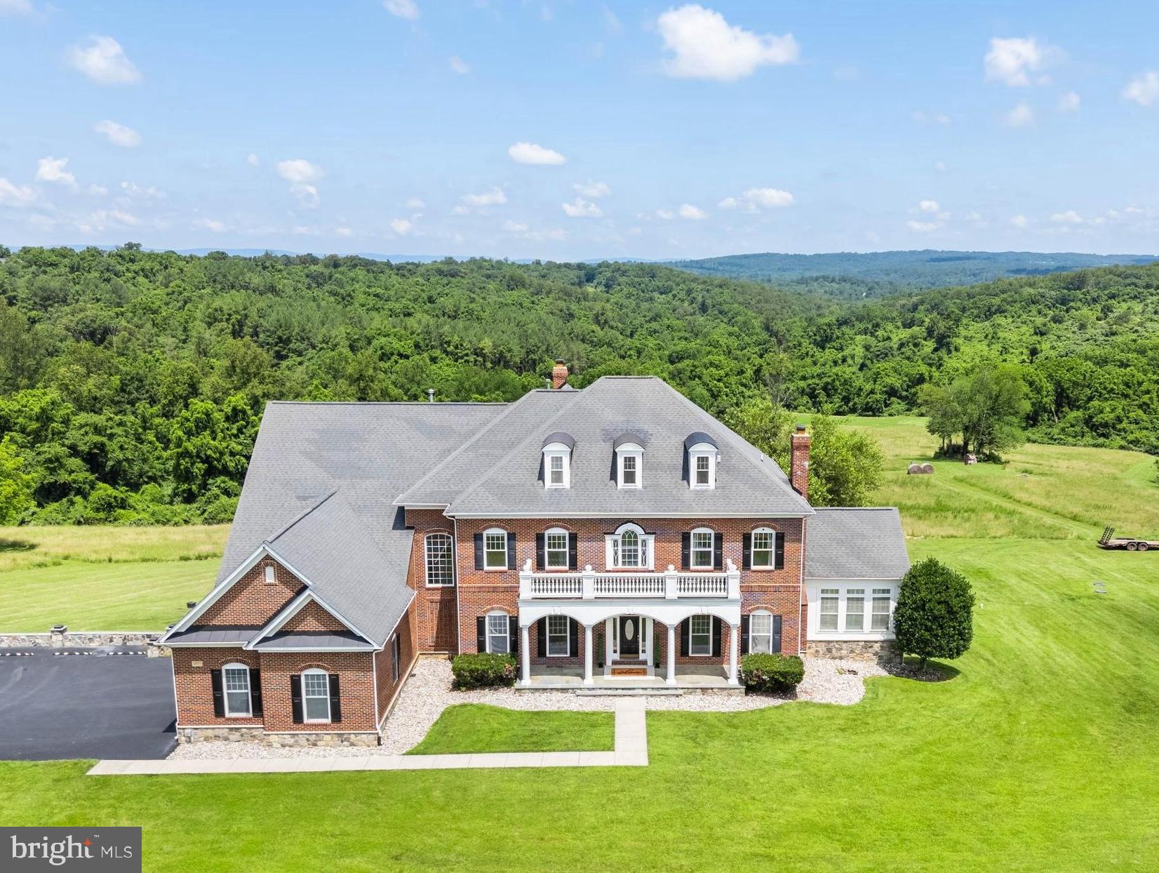 Classic. Impressive. Expansive. Secure.
This immaculate country estate is a rare offering in Loudoun County. Superbly located with quick access to commuter routes—just 30 minutes to Dulles Airport and 15 minutes to Leesburg and Middleburg—this is the epitome of gracious country living with everyday amenities close by. Perfectly sited on 25 acres of open land with stunning views, the stately brick Colonial offers 9,900 sq ft of finished living space across three levels. A flowing floor plan includes five ensuite bedrooms, a spacious primary suite, formal and informal living areas, and oversized windows that frame the surrounding countryside and distant vistas.
Enter the grand two-story foyer with a sweeping staircase. The formal living room is to the right, with the dining room opposite. Toward the rear, a relaxed family room with a wood-burning fireplace opens to a stunning room wrapped in windows with premium views—ideal for morning coffee or evening cocktails. A large office makes working from home a pleasure, but the pool views may encourage an impromptu workday dip. Host and Chef alike will appreciate the grand, functional and inviting kitchen, recently updated with a new Viking refrigerator and custom walk-in pantry with butcher-block counters. A Viking range, oversized island, bar seating, and granite countertops complete the space. Upstairs, the primary suite features new carpet and paint, a sitting room, spacious bath, and an envy-inducing custom closet. Three additional ensuite bedrooms offer privacy and comfort for all. Wired and equipped for entertaining, the integrated whole-house sound system lets music flow seamlessly throughout. Movie nights shine in the home theatre, outfitted with an Epson Home Cinema 5050UB projector and premium Marantz and Martin Logan surround sound. The lower level also includes a home gym, a fifth ensuite bedroom and flexible living space with a gas fireplace—ideal for a rec room, guest quarters, or an in-law/au pair suite. Outside, a newly renovated vanishing-edge pool invites relaxation, while open fields offer endless possibilities—gardens, hunting, or future equestrian facilities. A detached four-bay garage provides space for tractors, 4-wheelers, tools, equipment, and gear. An extensive custom surveillance system, whole-house generator, and hand-pump backup well ensure peace of mind and self-sufficiency. When life demands convenience but your lifestyle craves space and serenity, this extraordinary property delivers the best of both worlds.