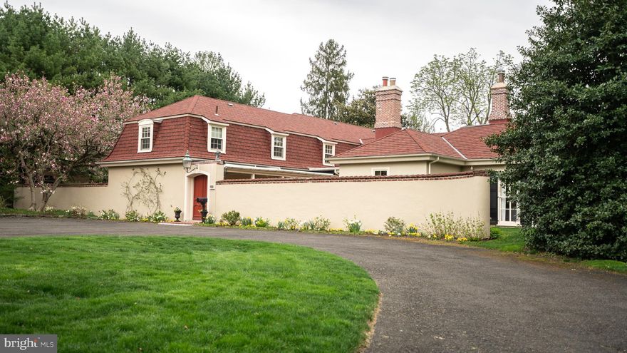 Thoughtfully designed by Walter Durham, this French Colonial home is an elegant original located on one of the nicest streets in Chestnut Hill. Details include built-in cabinetry, wood floors, Armoir-style wood doors, quality hardware, substantial crown moldings, and large, well-positioned windows that bring natural light throughout the home. The walled courtyard leads to a grand foyer with marble floors, a graciously curved staircase, and an attached powder room. The kitchen, recently renovated by craftsmen at Cullen, Inc., offers beaded inset cabinets, stainless steel and custom-paneled Thermador appliances, a breakfast room with access to a new patio, and a mudroom leading to a two-car garage. The living room is sunny and spacious with 11-foot ceilings and floor-to-ceiling windows. French doors open to the southeast facing patio, offering views of the one-acre lot and private frog pond. The living room has a wood-burning fireplace, while the welcoming study has a gas fireplace. The main floor master suite features a sunken tub and large walk-in closet with built-in storage. The second floor has an office/in-law suite living area and three bedrooms, each with an attached full bathroom. One bathroom was recently added and features new tile and vanity sink. The lower level is partially finished with a family room, a work room with laundry access, a Bilco door, and lots of storage. Located in a private setting, this gem is easy walking distance to Wissahickon Valley Park, Pastorious Park, The Philadelphia Cricket Club, Springside Chestnut Hill Academy, St. Martins train station, and Chestnut Hill's charming village shops and restaurants.  In addition to the renovated kitchen, there is a new roof, newer HVAC, and new windows on the second floor.