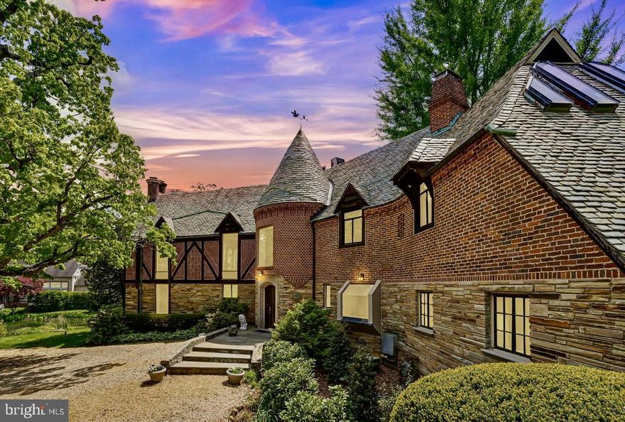 It’s rare to encounter a truly unique property—one that combines rich history, beauty, and elegance. 5908 Bradley Blvd in Bradley Woods is all that and more! Just moments from downtown Bethesda, this stunning property sits on approximately one acre, adjacent to a quarter-acre pond teeming with ducks, wildlife, koi, and surrounded by lush greenery and masterful landscaping.

The enchanting 1939 stone and brick Tudor was designed and built by Harry Edwards, the architect behind Greenwich Forest in Bethesda, as his personal residence. It was later owned by Michael Straight and Nina Auchincloss, the stepsister of Jackie Kennedy. This grand Tudor residence is a classic gem to be treasured.

The generously proportioned living room boasts an impressive fireplace, old-growth chestnut beams, high ceilings, and random-width oak hardwood floors. Floor-to-ceiling windows offer fabulous views of the pond and expansive gardens. The dining room, too, provides guests with a picturesque view of the gardens and pond and extends into a year-round climate-controlled sunroom through a wall of glass.

Upstairs, you’ll find seven bedrooms and six full bathrooms. The primary bedroom suite features two walk-in closets/dressing rooms and two full bathrooms. The lower level offers ample living space, including a sunlit library/office suite with a striking slate fireplace, built-in shelving, and access to a private patio.

This residence is filled with unique features, including a Y-shaped footprint that creates intriguing indoor and outdoor spaces, along with views of the surrounding gardens. The remodeled kitchen is equipped with a Thermador cooktop, Subzero refrigerator/freezer, and a double oven. The rounded breakfast nook, with its floor-to-ceiling window, overlooks a stone porch and perennial gardens. Newly installed landscaping at the front and back of the home is designed to maximize privacy.