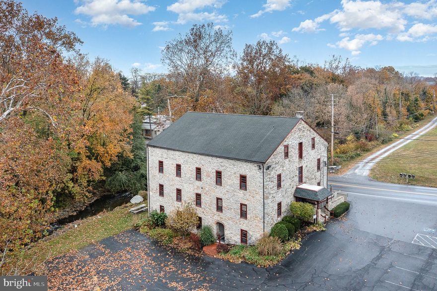 Discover a unique blend of history and modern functionality in this  converted historic mill, now transformed into an exceptional office building. Originally built in 1814, this property exudes timeless charm with exposed stone walls, high timber-beam ceilings, and  windows that flood each office with natural light and deep sills. The careful renovation has preserved its old world character, while adding contemporary conveniences like high-speed internet, energy-efficient lighting, and modern HVAC systems.Spanning a total 10,080 s/f, this building offers 3 floors of converted office space.  The main floor features an accessible floorpan, reception area, common work room, a kitchenette and 8 comfortable offices.  The upper floor provides 9 offices and a large conference room.   The lower level is separated, with its own private, accessible entry way and features an open floorpan with 7 offices, a conference room with a stone fireplace and mantle,  and room for storage.  This space is ideal for separate offices or subletting.  
Situated in Manheim Twp, this building is easily accessible, with ample on-site parking. Outside is a peaceful break area with picnic table overlooking the Conestoga River.  Ideal for businesses looking to inspire their team in a one-of-a-kind setting that balances history with innovation. Don’t miss the opportunity to own a piece of local history reimagined for modern business.