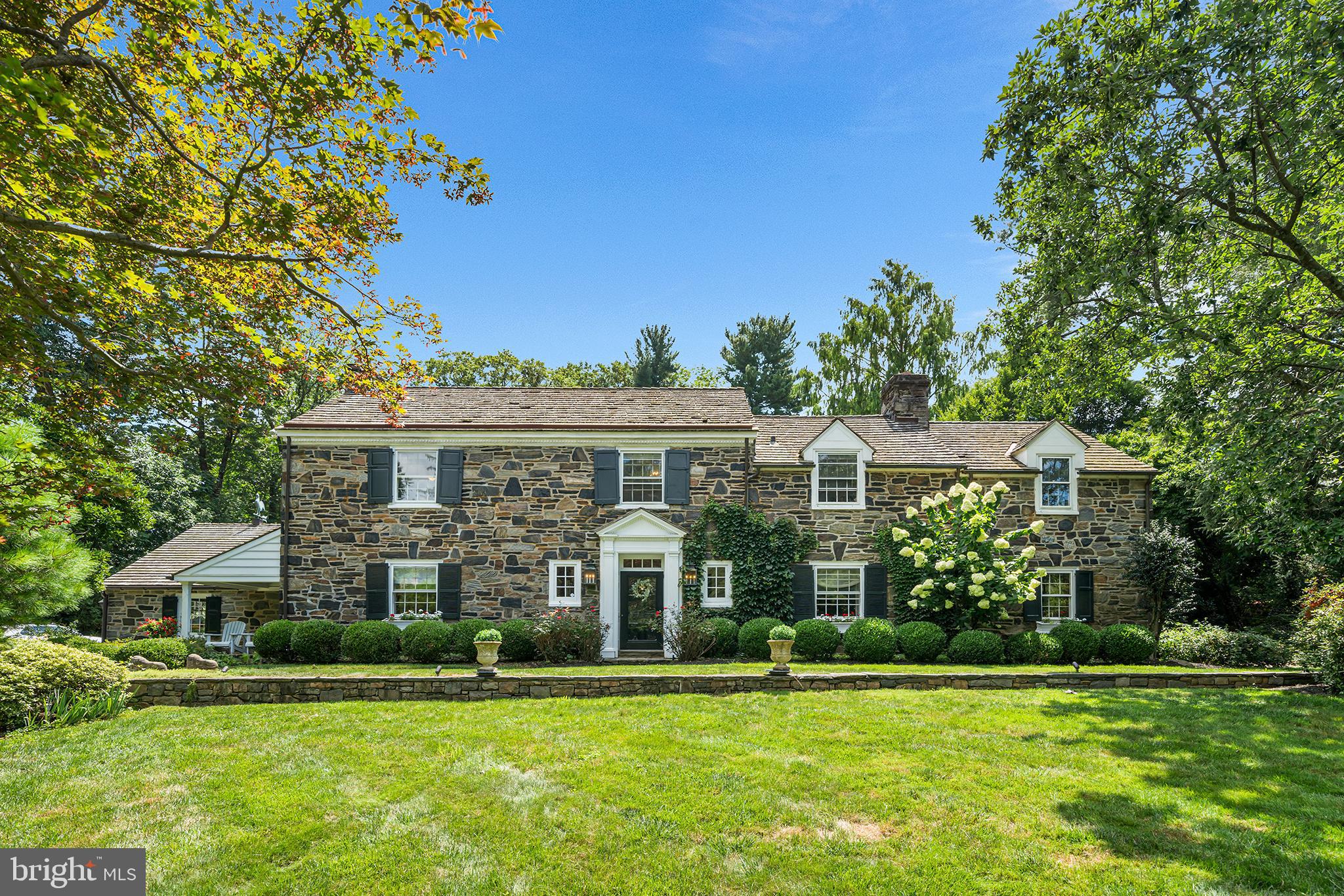 Welcome to this charming, classic stone home nestled in the serene enclave of St. Davids, where timeless architecture meets lush, storybook landscaping. With four bedrooms and two-and-a-half bathrooms, this residence is a rare blend of character, comfort, and thoughtful design. A winding stone pathway invites you in, surrounded by mature landscaping that rivals the gardens at Chanticleer—ivy-covered walls, colorful hydrangeas, and curated gardens set a picturesque tone from the moment you arrive.
Step inside to find a warm and inviting living room to the right, featuring rich hardwood floors, recessed lighting, a bay window, and a wood-burning fireplace with classic brick surround and a white mantle. Just beyond lies a cozy home office, complete with wood-paneled walls, built-ins, and stone flooring, plus access to a tranquil side porch.
The tiled eat-in kitchen is as stylish as it is functional, boasting a center Carrara marble island, counter seating, Wolf/Sub Zero stainless steel appliances, Stoltzfus cabinetry, and striking Julie Neill Alberto open cage lantern pendants. A charming circular breakfast table sits just off the kitchen, creating the perfect spot for casual meals. The kitchen flows effortlessly into a light-filled family room with cathedral wood ceilings, crown molding, and large windows overlooking the lush backyard. Throughout the home, all lighting fixtures and sconces are antique, adding to its refined character.
The formal dining room exudes elegance with wood floors, crown molding, a sparkling chandelier, and a bay window. On this floor, you’ll also find a beautifully appointed powder room, complete with a Celestine Basin from the London Basin Company and Sibylla wallpaper imported from London, as well as a mudroom designed for dirty boots and dog gear, accented by Clarke & Clarke wallpaper and anchored by a large armoire in place of cubbies. The main floor laundry room also features the same designer wallpaper, bringing a sense of cohesion and charm to these practical spaces.
Step out back to a stunning stone patio with a charming half-wall, surrounded by flourishing gardens—a true outdoor retreat for relaxing or entertaining. The backyard is a private haven, fully enclosed by a wooden fence, and features a 42-inch Pompeii-style brick pizza oven, a fountained lily pond with goldfish and frogs, and lush landscaping that creates a sense of tranquility and escape.
Upstairs, to the left, you'll find a Jack-and-Jill bedroom suite. The first bedroom features soaring ceilings and a ceiling fan, while the adjoining second bedroom offers an entire wall of built-ins with a convenient desk at the center—perfect for work or study. Down the hall is a third bedroom, currently set up as a home office with a daybed, highlighted by wall paneling and a ceiling fan. At the end of the hall, the spacious primary suite impresses with high ceilings, an exposed stone accent wall, and French doors that open to a private deck overlooking the backyard, complete with a circular staircase for easy outdoor access. The en-suite bathroom includes marble countertops, a soaking tub, an oversized glass-enclosed stall shower, and a towel heater, while the nearby walk-in closet offers generous built-ins for organized storage.
Other highlights include a cedar roof, indoor access to the two-car garage, and an unfinished basement accessed via the kitchen—perfect for storage or future expansion.
Located just a short walk to downtown Wayne, Fenimore Park (ideal for fishing and winter ice skating), and the scenic grounds of Eastern University with its peaceful walking trails and ponds, this home offers the tranquility of a luxury English village with the convenience of award-winning public schools and easy access to amenities. An absolute gem in one of the Main Line’s most coveted neighborhoods.