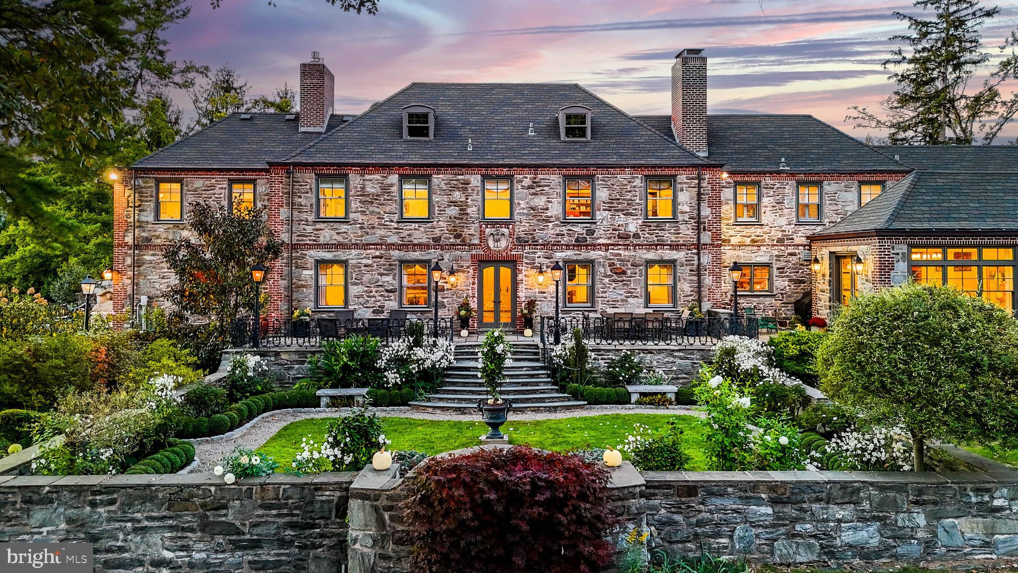 Welcome to Lionsgate at 620 N Spring Mill Rd, where classic architectural beauty & modern luxury converge in this magnificent stone manor house, restored by the present owners to its original grandeur. Built in 1929, it spans 10,664 interior sq. ft, with nearly 7,000 sq. ft. of exquisitely finished living space. Set on a beautifully landscaped and hardscaped 2.65-acre lot, featuring a large barn, gazebo, & secret garden, Lionsgate offers privacy & gracious living on the Villanova Gold Coast.
Drive thru grand stone pillars with a hand-carved lion’s head & gas lanterns and custom wrought iron gate to the stately house, accentuated with brick and masterful wrought ironwork by Samuel Yellin. Yellin (1884–1940) an American master blacksmith & metal designer, is renowned for wrought iron craftsmanship.
Once inside, the grand foyer with its elegant black and white checkerboard stone floor exudes timeless sophistication. The curved staircase, with Yellin rails, & large stained-glass window highlight architecture blending art & function.
The formal yet inviting living room, stuns with a hand carved alabaster mantle surrounding a wood-burning fireplace & deep marble windowsills. A majestic dining room with wood-burning fireplace, continues this theme, providing an elegant setting for family gatherings & dinner parties.
The cherry-paneled library offers a light-filled space for quiet work, with original wet bar, a third wood-burning fireplace with Valley Forge stone mantle & French doors leading to a stone terrace & sunken, outdoor hot tub with magnificent garden views.
An addition of informal living space by architect Ann Ledger, adds contemporary flair. The sun lit breakfast room, a custom wet bar, a dedicated computer or sitting area, tiled half bath & grand, yet cozy family room with fireplace & vaulted ceiling are perfect for relaxation. The kitchen invites culinary genius with Ethan Horowitz cabinets, double oven Dacor 6 burner stove & marble counter island.
Retreat to the second floor to discover the primary bedroom suite, with gas fireplace, walk in closets, and luxurious bathroom, with its own gas fireplace, air-jet soaking tub, French doors, and custom, wrought-iron balcony. There are four additional bedrooms, three with ensuite baths.
The functional lower level has a recreation area, powder room, exercise room & extensive storage solutions, including for wine.
Lionsgate’s exterior is a symphony of classic architecture and lush, thoughtfully curated landscaping, keeping with the caliber of this property. The rear exterior has a restored wraparound flagstone terrace with five gas lampposts overlooking a sunken “White Garden” surrounded by stone walls. The White Garden features a variety of white perennials for every season. The stately permanence of an old boxwood hedgerow leads to a Japanese Garden filled with azaleas, evergreens & Hakone grasses providing year-round color and texture.
Through a hornbeam archway and down a flagstone staircase, a particular highlight is the expansive lawn well suited for sports and play, with mature trees creating an idyllic park setting. Among these are numerous specimen trees including Coral Bark Maples, American Witch Hazel, Japanese maples, Styrax japonicus & Nellie Stevens hollies. Stately tall trees include majestic Red Maples, known for brilliant fall colors & broad canopies, & Yoshino Cryptomeria, Deodar Cedar, & elegant Eastern White Pines.
The charming post & beam barn, circa 2017, built with Canadian pine has two large garage bays, a potting shed & potential workshop. The Grand Gazebo serves as an outdoor living room for serene relaxation or al fresco dining. The secluded Secret Garden is a gem accessible through hedges. One can imagine a council of elves or hobbits meeting at the low table near the stone fireplace. Lionsgate is a testament to the art of living well, combining the grandeur of a bygone era with modern life. A story of luxury & enduring classical elegance.