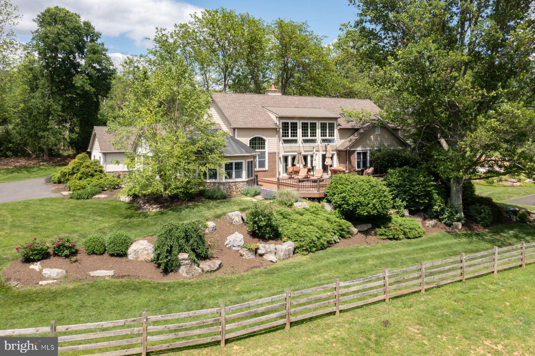 Nestled in a private enclave of just five distinctive properties, Hideaway Farm is a 13+ acre gentleman’s estate offering both serenity and possibility. Currently configured for equestrian living, the land is equally suited for transformation—imagine a boutique vineyard, an heirloom orchard, or a curated retreat space. This is one of Upper Bucks County’s most coveted hidden locations: private, scenic, and truly exceptional.
Originally a humble ranch, the residence has been artfully reimagined into a transitional Craftsman-inspired home that blends country charm with understated elegance. Every room enjoys captivating views—some stretching for miles and even more striking when winter reveals the distant hills beyond the treetops. Step inside to a generous foyer with vaulted ceilings and flagstone floors—a true greeting room that sets the tone for the rest of the home. To one side, a glass-wrapped office opens to a large deck, ideal for client meetings or creative sessions in a space that feels as inspiring as it is professional. The dramatic living room features a soaring two-story wall of windows, clerestory rain-sensor windows, a brick wood-burning fireplace, and newly refinished pine floors. Open to the dining room, this central space is perfect for entertaining. In warmer months, step out to the 1,200 sf multi-tiered deck for al fresco dining with views of horses at pasture and the sun setting over rolling fields. The kitchen is both charming and functional, with granite countertops, glass-front cabinets, and a brick accent wall. A center island with propane cooktop and a full Bosch appliance suite—including double wall ovens, microwave, and warming drawer—make this a chef’s delight. The adjacent breakfast room includes a wet bar and beverage fridge and opens to a bluestone patio shaded by an awning—perfect for morning coffee with birdsong and the gentle splash of a nearby fountain. The main-level primary suite is a private haven with double-door entry, long-distance views, and its own balcony overlooking the pool. The spa-like en suite features a walk-in shower, jetted tub, dual granite vanities, and a large dressing room with custom storage. Upstairs, a lofted family room leads to three spacious, light-filled bedrooms with generous closets and stunning views. One bedroom offers a walk-in closet, cozy window seat, and private bath, while the other two share a hall with double-vanity bathroom. The walk-out lower level is an entertainer’s dream—complete with a wood-burning stove, new luxury vinyl tile flooring, billiards area, and a curved granite-topped bar with wine storage and three beverage refrigerators. There’s also an exercise room with rubber flooring, and a full bath and spa tub for post-workout relaxation. Just outside, a heated dark-bottom pool offers an idyllic spot to unwind amid the lush, verdant surroundings. For horse lovers, the property includes a 6-stall barn with Dutch doors, dry lot paddock, tack room, 300-bale hay loft, hot/cold wash stall, and 10 acres of clover and orchard grass pastures enclosed by 4-rail fencing. An outdoor riding ring completes the picture for serious or casual riders alike. Beyond the formal pastures lies a lightly wooded sanctuary—ideal for campouts, quiet fireside evenings, or off-the-grid escapes on your own back 40. Despite its peaceful seclusion, Hideaway Farm is conveniently close to Saucon Valley, Bethlehem, and Easton’s vibrant dining and shopping. With easy access to farmers markets, the Saucon Rail Trail, and just 90 minutes to NYC or Philadelphia, this is rural luxury with a cosmopolitan connection.