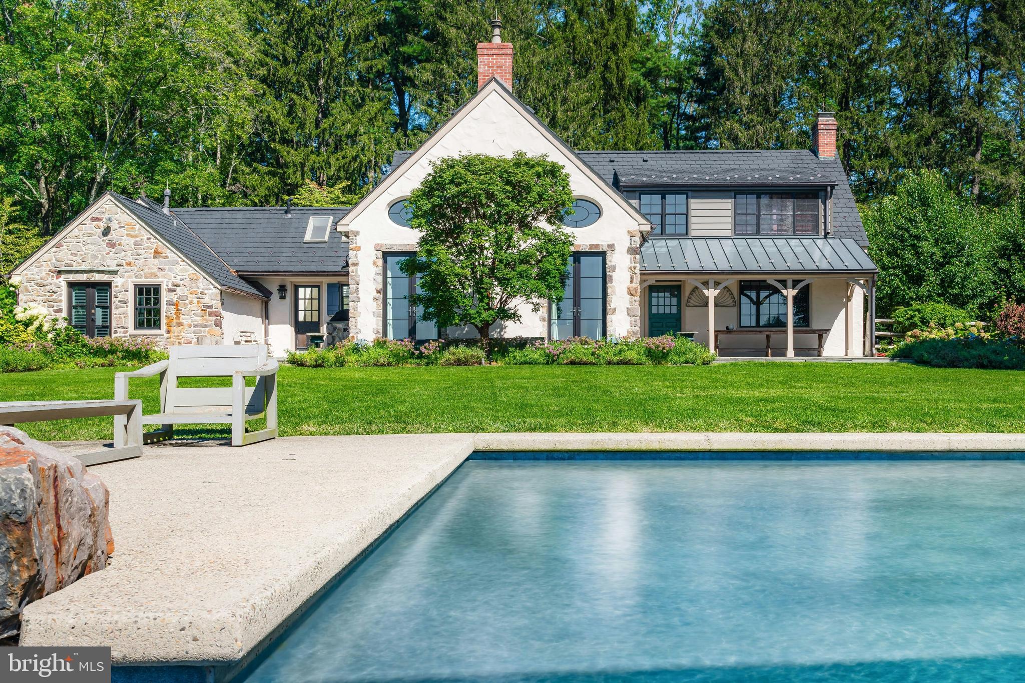 The winding country roads of Solebury Township are an idyllic backdrop for this elegant gated estate. Surrounded by twelve acres of rolling meadows and verdant woodlands, this bucolic property offers a serene and secluded retreat like no other.
Holmquist Farm epitomizes a harmonious coexistence between nature and the comforts of home. Every aspect of the property has been renewed or improved in the last three years, including stunning new floors and unique light fixtures throughout the main house, a detached garage with luxe guest house, extensive landscaping, infinity pool, and even a pickleball court.
Entry begins with a classic formal living room with deep silled windows, walls of built-ins, and a wood-burning fireplace. The large family room boasts a 2-story vaulted ceiling with reclaimed wood beams and massive chandeliers, along with a floor-to-ceiling stone fireplace flanked by tall windows. The 2022 gourmet kitchen is a chef’s dream, with marble backsplash, soft close cabinets, burnished bronze fixtures, and a large island. The dining room is elegant with hand painted orchids adorning the walls and French doors leading out to a bluestone patio surrounded by stately rows of flowering trees.
The luxurious first floor primary suite is a private oasis, with a high ceiling, lavish spa bath, and sliding glass doors to an ivy-draped patio. Upstairs, another full bedroom suite includes a built-in window seat, two Juliet balconies, and private bath, while two additional bedrooms share an updated hall bath. The finished lower level delights with a fully equipped wet bar, flex room suitable for a home office or extra bedroom, and wine room. A home theater, full bath, and stairs to the outside make this a wonderful space to entertain family and friends.
The grounds are ideal for entertaining or quiet days at home. Flowering trees and specimen plantings surround the home, while lush grass extends to a heated in-ground saltwater infinity pool with laminar jets. Surrounded by bluestone patios, this scenic overlook offers long-distance views overlooking open farmland and the hills and valleys of Solebury Township.
Across the driveway a newly built detached garage offers four bays with space for five vehicles. The upstairs guest apartment is an elegant residence on its own. An open-plan living area includes a full kitchen, positioned to take advantage of the oversized picture window looking out over the gardens. The custom marble backsplash is a work of art featuring flowering branches with dimensional marble petals. Two sunny bedrooms and a full bath are nearby, as well as a state of the art exercise room featuring a patented hardwood floor with subfloor spring mechanism and Nanawall that opens to the beautiful environs.
The property was once owned by Miss Karline Holmquist, founder of The Holmquist School for Girls, which merged with a local boys school to become the co-educational Solebury School, whose campus is located just up the road. Peace and quiet, a secluded haven within 90 minutes from three major metropolitan cities with access to international airports, world-class arts, cultural amenities, entertainment, shopping, and fine cuisine can all be yours at Holmquist Farm!