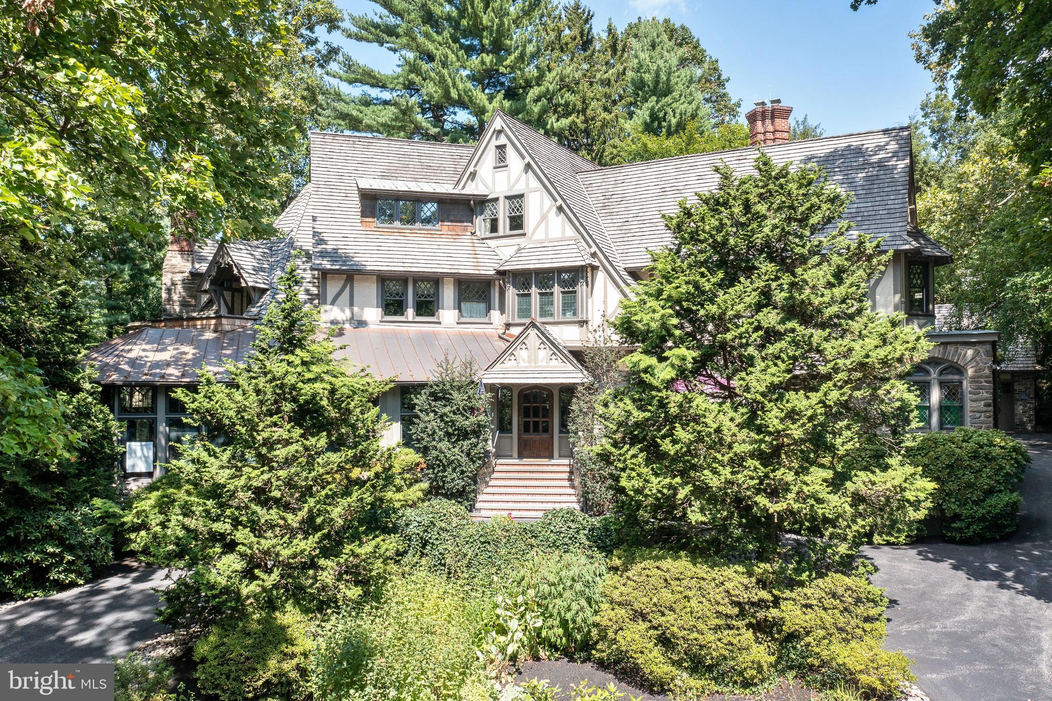 Follow the curving, tree-lined streets to your own private piece of history. Situated on a terraced southern slope in the South Wayne Historic District, surrounded by old-growth oak, birch and Japanese maple, Orchard Hill is an outstanding, meticulously maintained example of Tudor Revival architecture within easy walking distance of downtown Wayne and the St. Davids train station.
Comprising 3 parcels on nearly 3 acres, including 414 Orchard Way and 502 Meadowbrook Circle, the offering includes the main manor home, a carriage house, 2 detached garages and a lighted sport court on a separately deeded parcel zoned for another residential structure if desired.
From cylindrical stone turrets, gabled cedar shake roof and leaded glass casement windows; to its oak flooring; quarter-sawn oak moldings, wainscoting and millwork; and 7 unique fireplaces, every inch of the main home is simply gorgeous. Beaded copper roofing over the sun porch and rear overhangs adds drama. Designed by the firm of noted architect William Lightfoot Price and built in 1899, the impressive stone-and-stucco manor combines old-world elegance and exceptional craftsmanship w/ contemporary amenities and upgraded utilities for maximum comfort and ease of living. The approximately 10,000-sf home features 16 rooms, including 5 bedrooms and 5 baths on its 3 above-ground floors.
Off the circular drive, a gabled oak entryway opens to a large center foyer. To the left, an arched doorway leads to a spacious living room with vaulted ceilings and original stained glass windows. The room’s focal point is an elaborately carved stone mantel featuring a pastoral tableau over 1 of 4 gas fireplaces on the first floor. Two sets of stained glass double doors provide access to an enclosed sunroom overlooking the flagstone patio and wooded grounds. And you’ll find a perfect spot for reading on a cushioned bench under the domed ceiling in the library/turret room, which features stained glass windows and curved bookshelves.
The living room also opens to the John Milner-designed eat-in kitchen, built by EB Mahoney, with Coventry cabinets and 2 dishwashers for holiday meals and large gatherings. Off the kitchen is a formal dining room w/ cozy alcove dining nook. The lower level has an 800-bottle climate-controlled wine cellar with soapstone countertops, Chicago brick and reclaimed French terracotta, Amish woodworking and hand-forged metalwork. A 2-story addition built in 2003 added a powder room, second office, mudroom and second-floor craft room/office adjacent to a large laundry room with linen closet.
Upstairs, escape to the primary bedroom suite, w/ 2 renovated en suite bathrooms, fireplace, custom closets, a window seat and both sunrise and sunset balconies. Two other second-floor bedrooms each have an adjacent full bath in the hallway, and the second floor is accessible from the foyer or kitchen. The third floor, with its architecturally unique rounded ceilings, has two additional bedrooms and a hall bath, as well as a sitting room/playroom and an air-conditioned attic with original built-in storage cabinetry. Second- and third-floor guest bedrooms also feature fireplaces, and some have generous window seats.
Throughout the home, main fixtures and utilities have been updated to include natural gas heat, central air and 400 amp electric, w/ a natural gas-powered back-up generator. It also boasts a water-softening system, wiring for electric vehicles in the 3-car main garage and commercial hi-speed WiFi throughout the compound.
Ideal for guests, in-laws or rental, a 2-story carriage house with slate roof has 2 upstairs bedrooms, plus a full bath on each level. It offers a remodeled kitchen and a spacious living room with new flooring, built-ins and a beamed ceiling. It also houses controls for the heated saltwater pool with fountain, built-in spa and retractable cover. Carriage house has a 2-car garage w/ attic space.
Orchard Hill is in the highly desirable Radnor Schools.