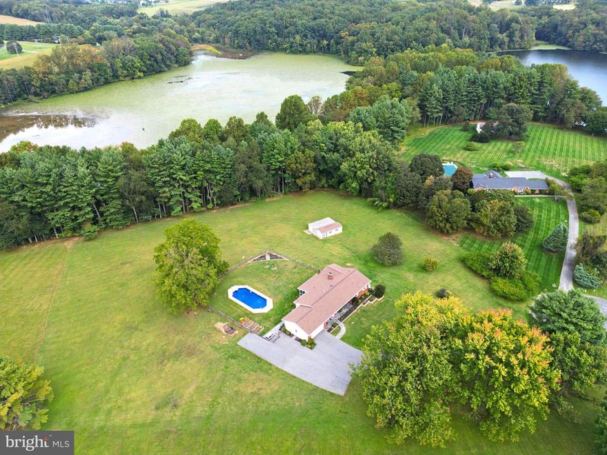 Peacefully set on a secluded and private lot, this beautifully maintained ranch-style residence rests on over 3 sprawling acres in the serene Candlewick community, backing directly to Piney Run Lake. Lush front landscaping, garden walls, and a wide front yard create a welcoming first impression, leading to a charming front porch. Step inside to find gleaming hardwood floors and a traditional, thoughtfully designed layout. The main level begins with a foyer that opens to a formal living room with bow windows, and a formal dining room that flows into a sunny breakfast area. A nearby mudroom/laundry room offers convenient side exterior access. The gorgeous kitchen features upgraded countertops, an island, and stainless steel appliances, and opens seamlessly to the inviting family room. Here, a gas fireplace with a brick surround, built-in bookcases, and sliding doors to the screened porch create the perfect setting for everyday living or entertaining. Hardwood floors continue throughout the main level, which offers three spacious bedrooms, including the primary suite with a private full bathroom, three closets (one walk-in), and its own exterior access. A second full bathroom with a dual-sink vanity completes the main level.
The finished lower level, updated in 2022, provides exceptional flexibility with a recreation room featuring an extra-large wood stove set against an exposed brick corner wall, luxury vinyl plank flooring, and a full kitchen. A bedroom with two closets and a full bathroom with a roll-in, handicap-accessible shower makes this level ideal for an in-law suite or guest quarters. There are also three unfinished rooms—two utility rooms with storage and one additional storage space—offering ample room for organization and projects. Outdoor living shines with a screened porch overlooking the expansive backyard, complete with a fenced in-ground pool, garden boxes, and a storage shed. The property backs directly to Piney Run Lake, offering a peaceful, private setting surrounded by nature. Recent updates include: HVAC system (2 years), fence (2 years), storm doors (5 months), well pump (3 years), roof (3 years), gutters and windows (3 years), sidewalks (3 months), pool liner (2 months), driveway paving (4 years), and hot water heater (6 months).