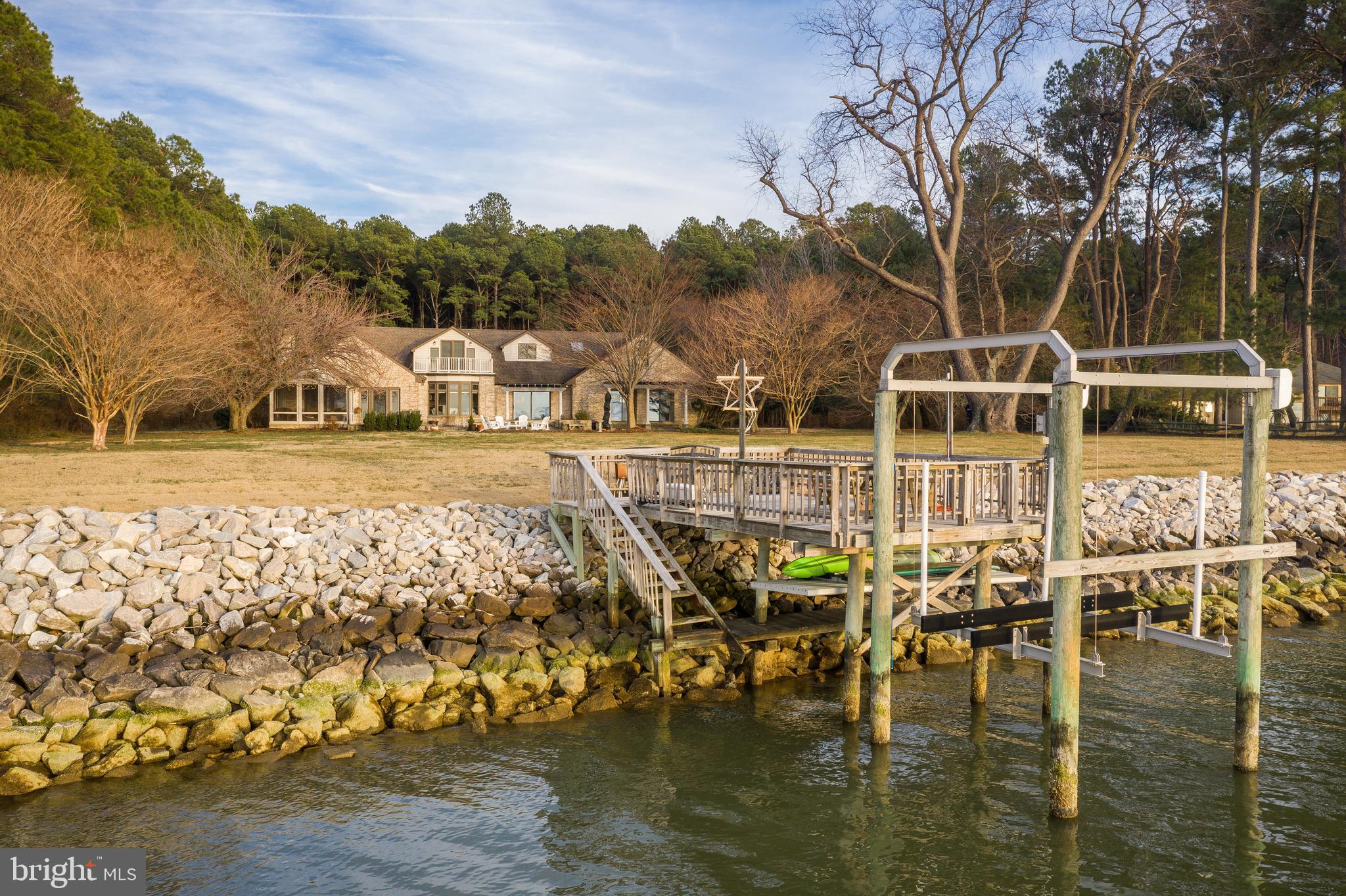 Offering panoramic views of Eastern Bay and beautifully situated on 10.8 acres, this 4400+ sq. ft. home is traditional and elegant yet woven with a casual vacation vibe of being right on the water. Step inside and experience the stunning water views throughout, gorgeous millwork, and handsome hardwood floors. A beautifully thought out and expansive floor plan allows for incredible entertaining inside to out. Start with the lovely waterside living room that opens to the deck and move on to a stunning oversized gourmet white Chef's kitchen with high-end appliances, center island, water views and all open to the large and cozy family room with a wood burning fireplace flanked by custom built-ins and access to the screen porch and deck. An elegant formal dining room with a curved entryway off the foyer will be the gathering place for holidays and special occasions. After a busy day, retreat to the main level primary suite with two walk-in closets and double sets of doors to the waterside patio, along with a spa-like bathroom with jetted tub, walk-in shower and two vanities. Find three additional bedrooms, one ensuite, a hall bathroom and a powder room on this level. A convenient laundry/mud room is just off the garage. The fabulous upper level offers the perfect flex space! A large second family room with skylights and a balcony overlooking the water, a bonus room and a full bathroom offer endless possibilities. The outdoor features of this property are a waterside mecca. Pull your boats into the private pier with 3’ +/- MLW, 2 slips and a boat lift. Enjoy those Eastern Bay breezes sitting on your screened porch or gathered on the deck with built-in seating or the patio. Just a short drive to either St. Michaels or Tilghman Island, with plentiful dining and shopping venues.