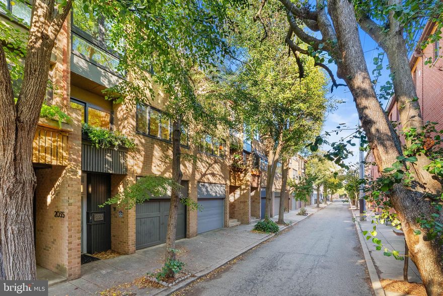 Beautifully maintained contemporary townhouse on a quiet, tree-lined street in Rittenhouse. This light-filled home features a multi-level layout with dramatic ceiling heights and sweeping city views. A spacious entry foyer offers a large coat closet and direct access to the attached garage, now equipped with a dedicated EV charger for convenient at-home charging. The finished lower level includes a bright daylight den and powder room, ideal for a home office or guest space.
The main living area boasts 13’ ceilings, oversized windows, and a gas fireplace, with French doors leading to  an expansive private rear patio and garden—large enough to accommodate a full outdoor dining set, lounge seating, grill area, and container gardens—creating a true extension of the living space and perfect for entertaining or relaxing outdoors.. The dining area overlooks the living room, creating an open and airy feel. The updated eat-in kitchen opens to a south-facing balcony, perfect for plants or morning coffee, and a versatile loft space overlooks the main living area. Upper levels include a spacious primary suite with ample closets and an en-suite bath with double vanity, plus two additional bedrooms and an updated hall bath with laundry. Located in the Greenfield School catchment and minutes from Rittenhouse Square, parks, dining, and shopping.