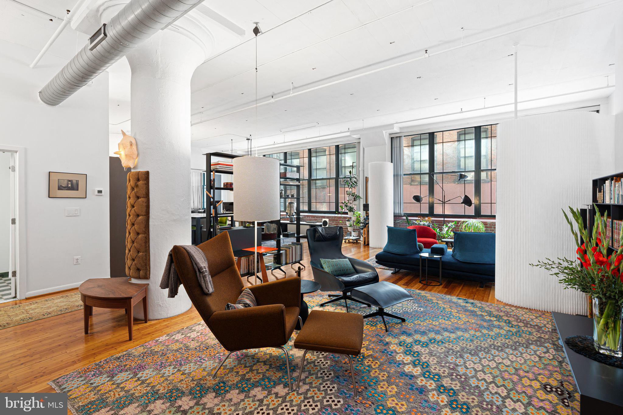 This unit is a rare find in Philadelphia, a loft in the truest sense—open, expansive, 2,000 square feet with warm wood flooring over solid concrete, exposed brick, light and air that move easily through the space. Ceilings stretch nearly 12 feet, windows run wall to wall. Bring in all your beautiful things, or keep it sparse and let the light do most of the work. Flexible partitions let you carve out space when you need them, and disappear when you don’t. The rest of the apartment follows that rhythm. Big enough to adapt. Minimal enough to stay calm.
The kitchen is the natural center of activity, Italian-crafted and designed to draw people in. Poliform Varenna cabinetry keeps the lines clean, quartz counters wrap an island that doubles as a bar-height table, and built-ins stay quietly out of sight. It opens into the dining area—good for dinners that run late with friends, or quiet nights with just a bottle open and music low.
The primary bedroom suite is larger than many full apartments, with a dressing area and custom wardrobes to keep everything in place. The owners’ bath is generous, appointed with materials that are both contemporary and timeless. An oversized shower, a soaking tub, a floating vanity—details more considered than flashy. An artist-made textile screen here, sliding moiré doors there, touches that add texture without demanding explanation.
Outside, it’s Philadelphia at its most livable. You can walk to galleries, music venues, Chinatown noodles, coffee, beer halls, climbing gyms, the Rail Park. Condo fees are refreshingly low for a space of this scale, a rare bonus in a building like this. SEPTA’s close if you need to move farther. But most of the time, you probably won’t.