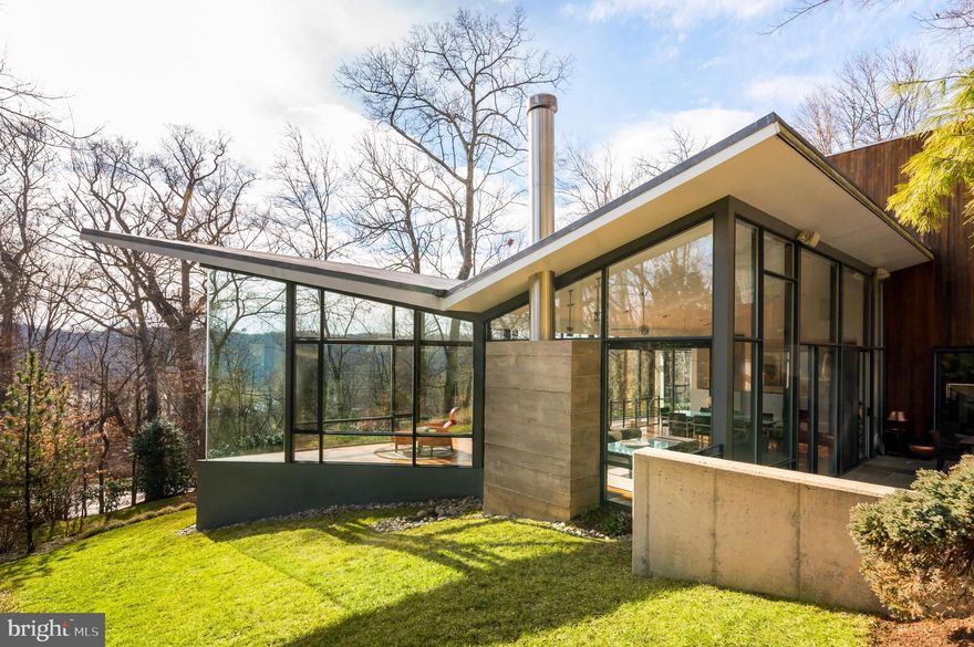 If you want to live in a one-of-a-kind piece of art, then this is the home for you!  Perched high on a wooded lot overlooking the Potomac River, 5300 Mohican Road stands out amongst the  homes of Glen Echo as a stark juxtaposition and iconic symbol of avant-garde contemporary architecture. Equal parts function and pure artistry, this masterclass in design was the brainchild of visionary architect Robert Gurney, FAIA, and the recipient of numerous international aesthetic awards. Harmonious with both itself and the surrounding landscape, the home is honed from intersecting spatial volumes and a diverse palette of materials adaptive to changing light and shadows, establishing the structure as one with the site. Entry is provided via a striking elliptical tower clad in lead coated copper, nestled within a rectangular, mahogany-clad mass tapering into the recognizable glass triangle. Within, the eye is drawn upwards by the sweeping maple staircase and perforated aluminum bridge overhead, while light floods in through the skylight above. The whimsical interiors are a wonder in circulation and inviting the outdoors in. An open living and dining space is surrounded by three sides of glass and topped with an upturned butterfly roof. Such design enables truly stunning scenery encompassing roaring waters, radiant sunsets, and twinkling Tysons Corner skyline in the distance. Verdant greenery envelops the space, establishing complete privacy and tranquility. Brazilian cherry floors emit a warm glow in the natural light and reflect the wooded surroundings. Various metals, board-formed concrete, Venetian plaster, exotic woods, and glass come together in a beautifully contrasting yet harmonious fashion, instituting a distinct identity within. Separated by a tempered-glass panel, the commercial kitchen’s custom mahogany cabinetry houses Viking, SubZero, and Thermador appliances. The primary suite occupies its own wing with private office, double-sided wood-burning fireplace, sumptuous spa bath with custom millwork and concrete counters, as well as a double dressing room. Three additional bedroom suites are privately tucked away. Luxurious amenities abound, including a state-of-the-art media room, professional fitness center with steam shower, sauna, and indoor/outdoor hot tub, and a fully automated audio-visual suite. A Bluestone terrace is built into the hillside adjacent to the glass living room, providing sheltered outdoor living and enhancing the relationship with the inside. 0.54 acres of land offers ample cushion and a serene natural retreat. A one-of-a-kind offering which truly cannot be replicated, 5300 Mohican Road is one of the Capital Region’s most special residences.