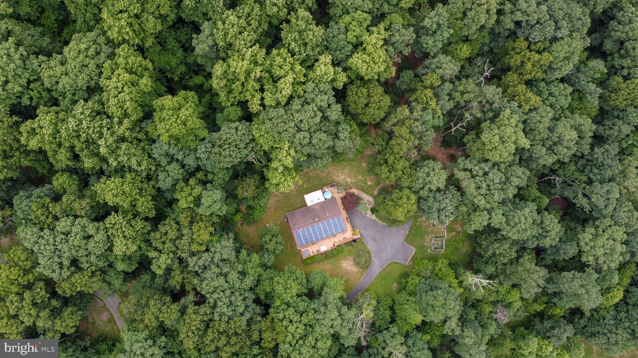 Situated on a long tree-lined driveway at the end of a private road, this two-level rancher is built on a 9.44 acre wooded lot on the east slope of Braddock Mountain, only ten minutes from shopping and dining in downtown Frederick, and hiking at Gambrill State Park. The main level includes a kitchen with solid cherry counters, and large east-facing windows with a view of the sunrise and nighttime views of the city lights, 700 feet below. The living room has a cozy propane fireplace, and two sunny offices fill out the living area.  Symmetrical gigabit internet service is available, making this a perfect remote work retreat.  A 15x12' gas heated sunroom is attached to the living room and rear deck, which wraps around half of the home! The home has a primary suite with large bathroom, plus two guest rooms that share a single full bath in the middle of the home.  Warm wood trim and large entryways throughout compliment the home's forest setting. The lower level consists of a long garage that runs the full 52' length of the home, with built-in workbenches and heavy duty shelves.  The remainder of the lower level includes a workshop, exercise space, and a high-end home theater, which is fully included at asking price. A roomy half bath is attached to the theater room, with space to add a shower. Home's website includes details of the theater room, as well as well water reports and other information.  Storage space is plentiful, between the garage, several closets on the lower level, and a walk-up attic with full floor. The sloping, private lot is covered with mature hardwoods and a fire pit area, where you will spot deer, turkey, fox, and even the occasional black bear and bald eagle! A large parking area on the paved driveway has space for 6 cars.  There is a deer-proof raised bed garden, and herb boxes scattered along the large wrap-around deck, along with a hot tub in a custom built surround.