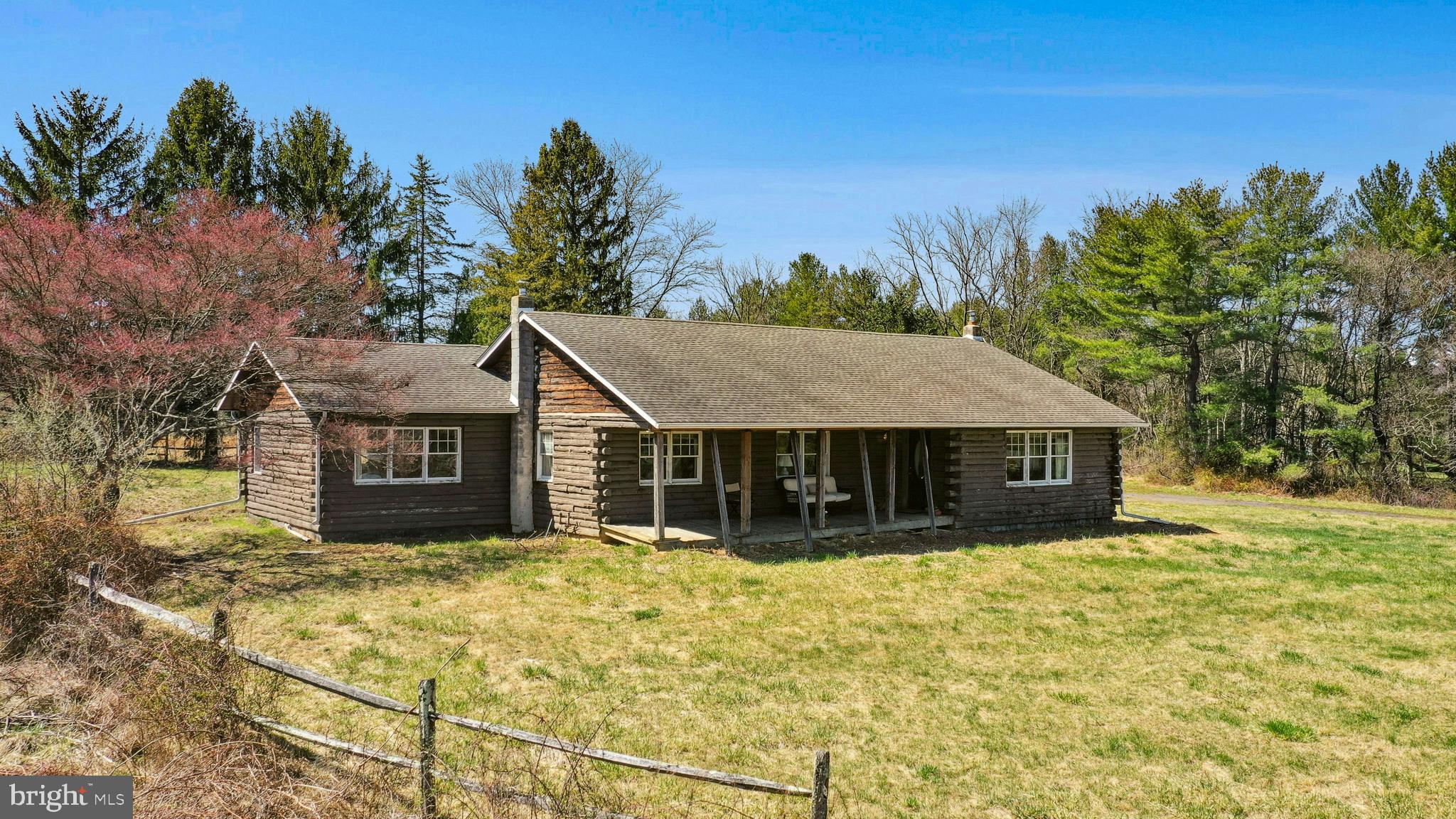 An incredible 360° panoramic view in the rural setting of Durham Township, this private estate is set on more than 15 idyllic acres. Boasting a log cabin, detached extended height garage, and a 3-stall barn, Lallystone Farm is an excellent opportunity for homesteaders, equestrians, or weekenders.
Situated back a long tree lined driveway, the single level log home was built in 1986 and remodeled in 1994. Gleaming hardwood floors are set off by abundant windows, with long range views from every window. The kitchen offers wood cabinets and a full size side-by-side Subzero refrigerator and freezer, and opens easily to the cozy breakfast area. From here the living room is generously sized, with a wood-burning stove and access to a covered porch. The primary suite is joined by a hall bedroom, office, and powder room. Upgrades like, oil furnace replaced in 2020.
The 2-car detached garage offers an oversized bay door and extended ceiling height for larger vehicles. Nearby, a dry paddock leads to a 3-stall barn with tack room, electric, and water. Excellent location, views and privacy make this the perfect project for those looking to create a Bucks County estate of prestige. Protected from the road yet close to commuter routes, shopping, and dining, Lallystone Farm is ready to welcome its next caretaker.