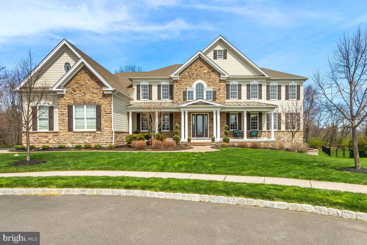 Located at the end of the cul-de-sac, this gorgeous 5 BR stone-front Henley model in desirable Chapman’s Corner features a first-floor bedroom suite!
A transitional home and floor plan with hardwood floors and fine appointments throughout. In the welcoming, bright entry is a dramatic butterfly staircase, the central focal point in the reception area. The home’s inviting spaces, including its formal living and dining rooms, are finished with detailed millwork, crown moldings, raised panels and plenty of windows, creating light-filled rooms with timeless appeal. Just steps away is the entrance to a lovely, expansive ensuite with sitting area. Nearby the beautiful formal dining room has easy access to the kitchen. This space, suitable for the gourmet and the everyday, features a granite center island and breakfast bar, walk-in pantry, casual dining area and easy access to a full mudroom from the garage. The kitchen and deck views look over the lush, green fenced yard with peaceful natural views of protected open space. The two-story family room with stone-front gas fireplace is a comfortable space to nest in any time of year. For work and study there is a handsome executive home office with stunning custom cherry cabinetry and bookcases. A powder room is nearby. The second level features an open landing with a gorgeous main bedroom suite with sitting room and two of everything: his and her spa bath with jetted tub and his and her water closets, and a superb his and her walk-in closet. The second level features three additional lovely en-suites and a convenient laundry room. An unfinished lower level is beyond expansive and features nice walkout access for play or outdoor activities and plenty of storage. This area can be customized to your specifications: Create a media room, wine cellar, gym or all of them! Basement refrigerator is included. Three-car attached garage has high ceilings and additional storage. Whole-house generator, interior sprinkler system, stucco mitigation with warranty transferable to new owner. Close to Newtown, shopping dining, Council Rock schools, Easy access to I-95 to NY, Philadelphia, NJ. This exceptional offering is move-in ready!