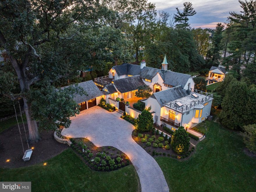 Tucked behind gates on two private acres in Villanova, Au Vallon reveals itself slowly, like a secret estate in the French countryside. The 150-year-old carriage house, whose name translates to “In the Valley,” has been expanded and reimagined with a sense of restraint and reverence. Its original stone walls and hand-hewn beams remain the anchor, while light-filled glass courtyards, sweeping terraces, and finely detailed additions create a home that feels both historic and current.
The present owners have undertaken a thoughtful transformation, guided by the principle that every improvement should be worthy of the home’s origins. Their work—ranging from a newly built pool house with outdoor fireplace to a three-car garage fitted with sculptural hydraulic doors—was carried out with the same level of craftsmanship that defined the original construction. The result is an estate where modern comforts are seamlessly integrated into the existing architecture, and where new layers of design feel sympathetic rather than imposed.
Inside, the rooms unfold with a natural rhythm. The formal living room, with its built-in shelving, elegant fireplace, and French windows opening to the gardens, sets a tone of understated grandeur. Beyond a hidden bookcase door lies the dining room, where a carved mantel and French doors connect the space to the slate terrace and Linden allée. The family room, crowned by vaulted beams and a stone fireplace, is paired with a country kitchen of true scale: granite countertops, dual Sub-Zeros, a Wolf range, two dishwashers, heated floors, and a walk-in pantry designed to support both intimate meals and large gatherings.
The private quarters are no less compelling. Each of the five bedrooms is en suite; several include fireplaces, balconies, or terraces overlooking the landscape. The primary suite, a study in proportion and light, offers beamed ceilings, a Juliet balcony with views of the pool, and a bath conceived as a retreat—freestanding tub before the fire, glass-walled shower, cedar sauna, and dual vanities discreetly divided for privacy. A wood-paneled bedroom with Mercer-tiled bath speaks to the home’s history, while the lower level extends the living experience with a guest suite, second sauna, gym, and direct access to the pool.
Outdoors, the gardens are composed with an eye toward both structure and romance. Specimen plantings dot the grounds, while clipped Linden trees form a shaded dining canopy reminiscent of Provence. Slate patios, balconies, and roof decks create multiple vantage points to experience the property. The pool, recently restored, is a focal point, animated by a sculptural fountain and complemented by the pool house.
At Au Vallon, the past has not been preserved behind glass but rather allowed to evolve—its early 19th-century bones guiding a vision of 21st-century living. The estate stands as an architectural dialogue across centuries, offering privacy, beauty, and a sense of permanence that is increasingly rare.