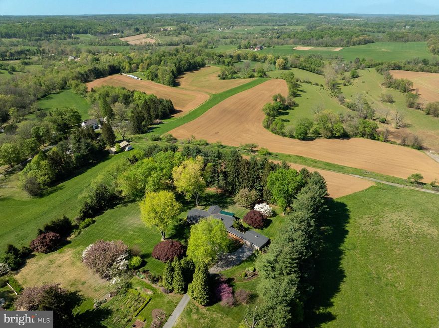 372 Lucky Hill is a private custom Ranch Retreat nestled on 2.7 lush Chester County acres in the gorgeous countryside of East Bradford township!  Minutes from bustling downtown West Chester, you will be amazed at this private country setting with magnificent gardens and specimen trees, most notable is the Japanese Maple. Surrounded by protected farmland and the 500-acre Stroud Preserve across the street, the views are spectacular! In a small exclusive development of three properties, this custom home is oriented to take maximum advantage of its setting. It is set far back off the road on the largest of the three parcels and protected by a lush canopy of nature. The character and flow of the home will win you over, especially the massive stone fireplace and gorgeous views out of every window! Enter the foyer and notice the fine Italian marble floor and handsome hardwoods. The updated Kitchen is off the large Living Room with high ceilings, stone fireplace and access to rear covered deck. There is a library nook leading to the Family Room/Den/Formal Dining Room, expanded by the owners, with a corner fireplace.  This was originally used as a bedroom and can be converted back. It has access to an updated full bath with double sinks.  The spacious primary bedroom has access to two full baths, a dressing area, ample closet space and rear deck access.  There is another bedroom with full bath access off the foyer. A hall powder room completes this level. The finished lower level was waterproofed and finished with a spacious game/entertainment room, bedroom with access to full hall bath, home office and utility room and storage.  Numerous updates include water purification system, new hot water heater, new roof, updated Anderson windows, updated baths and many more! A charming, covered walkway offers access to the detached 2-car garage.  The deck is wrapped around the rear of the home, with fine views of this nature-lovers paradise!  Notice the carefully planned old growth trees, shrubs, plants and flowers, which will wow you in every season.  Walk to the rear of the property and peer through the large screen of evergreens for a bucolic view of the neighboring farms. Properties with a unique sense of place like this do not become available often!