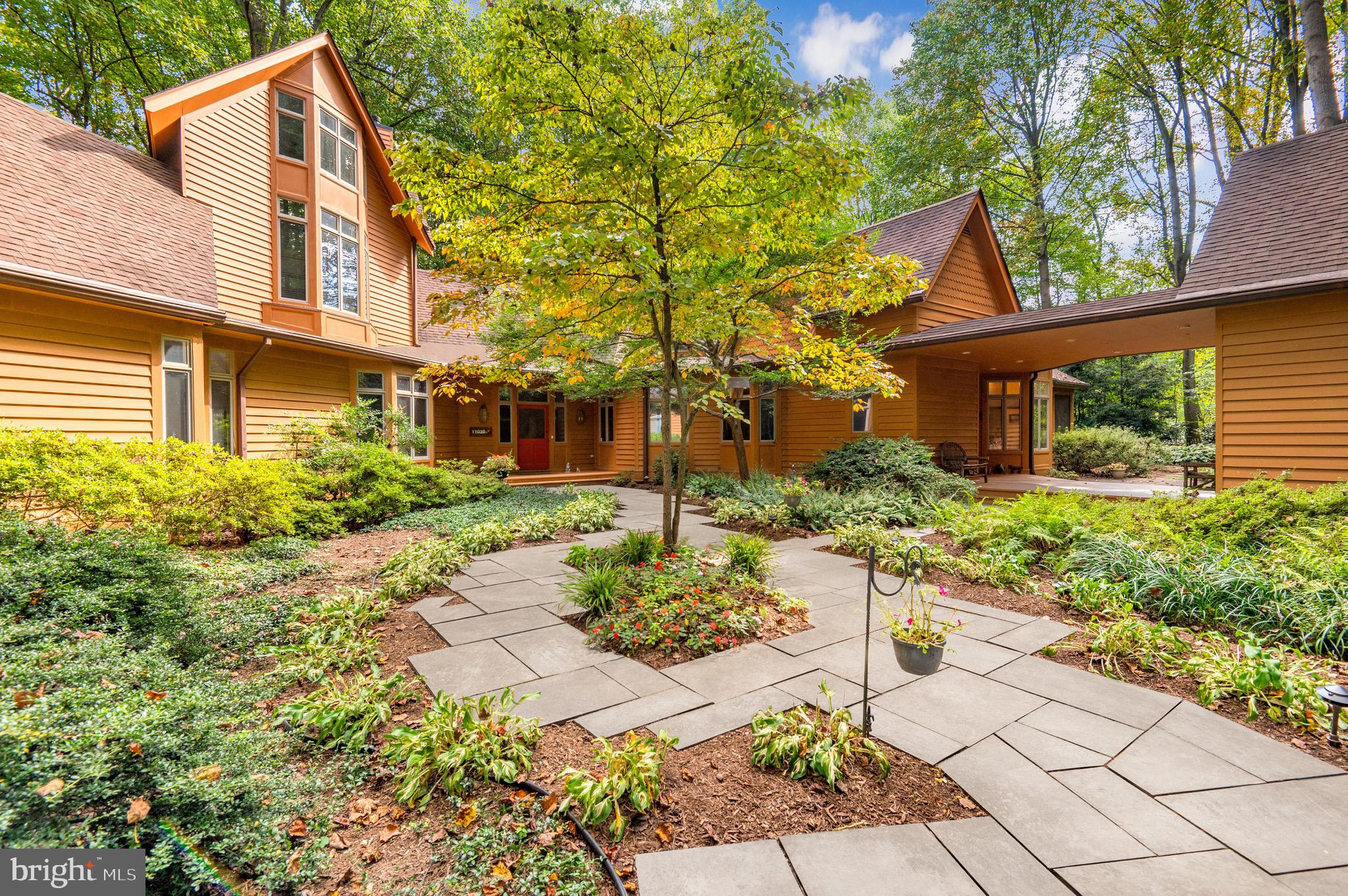 Welcome to 11036 Dobbins Drive, a private retreat nestled on two and a half acres of meticulously landscaped gardens in Potomac, Maryland. This custom-built residence highlights four bedrooms, three and a half bathrooms over an impressive 5,100 square feet of living space. Designed with expansive open areas, bathed in natural light, and bedrooms thoughtfully placed on the main level, this property distinguishes itself as a unique and rare find in the Potomac area.
Journey along to the gated entrance, where an enchanting display of trees and gardens surround the circular driveway. The wood exterior and plethora of windows enveloping the home will instantly capture your attention. Follow the flagstone walkway to the covered front porch to enter the front of the home. A beautiful foyer with elevated ceilings and curved hallways greet you to take you to each main level offering. The windows throughout the home offer an immersive nature experience, blurring the lines between indoor comfort and the beauty of the outdoors. The sunken great room impresses with vaulted ceilings and panoramic wooded views through the oversized windows adorning the rear of the home. A wood burning fireplace takes center stage and access to the outdoor patio can be found through the glass doors.
This residence is an entertainer's delight, boasting a magnificent dining room that effortlessly flows into the butler's pantry for seamless entertaining. Guests can savor the stunning garden views from the dining area, making every meal picturesque. The kitchen was tastefully designed with a spacious center island, ample cabinetry, a walk-in pantry, built-in shelving, and a cozy breakfast nook set against a bay window. For al fresco dining, step into the screened porch, equipped with a ceiling fan, which leads to the inviting wood deck. A practical mudroom is strategically located by the side entrance, equipped with a main level washer and dryer, while an adjacent room houses a built-in office area. A captivating library area lies further down the hall, featuring a wood-burning fireplace, surrounded by custom shelving and cabinetry. This space offers an idyllic setting for a work-from-home office. Additionally, the foyer is flanked by a discreet powder room and an oversized hall closet, ensuring storage for your everyday items.
The main level graciously accommodates three bedrooms and two full bathrooms. The primary suite is a sanctuary of comfort, bathed in natural light from the surrounding windows that frame the private wooded views. Complete with built-in shelving and cabinetry, there is a space to store any item. The en-suite bathroom showcases dual vanities, walk-in shower, and an indulgent tub. A convenient vanity area connects to a generously sized walk-in closet, equipped with a built-in safe. Two additional bedrooms, wrapped in wooded views, complete this level, providing cozy retreats for family members or guests.
Ascend the hardwood staircase to the upper level, where you'll discover a distinctive loft area with vaulted ceilings and breathtaking treetop vistas. This versatile space serves as an additional living area, perfect for lounging while enjoying the scenic surroundings. A full bathroom and closet are located on this level, while a generously sized storage room offers space to stow away larger items.
Behind two wooden doors just off the main foyer lies a hidden gem - a staircase leading down to the unfinished lower level. As you descend, anticipation builds for the possibilities awaiting your creative touch. With its walk-out entrance to the backyard and generously sized windows letting in natural light, this space brims with potential.
Outside, the beautifully landscaped lot unfolds with multiple gardens, a flagstone patio and deck providing a serene setting for outdoor gatherings and relaxation. This remarkable property is ideally situated, just minutes from Potomac Village, the Cabin John Shopping Center, and with easy access to bo