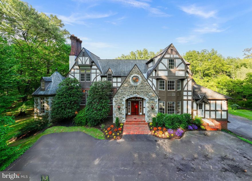 Impressive Tudor estate located on the quiet little segment  of Old Gulph Road in a prestigious neighborhood on 
a picturesque 1.1-acre lot overlooking Mill Creek in Northside Bryn Mawr. Designed by Peter Batchelor and built by E. Allen Reeves in 1993, this architectural gem earned the Merit Shop Award of Excellence for superior craftsmanship and design.
Arriving via the inviting circular driveway, you are greeted by the elegant front facade with stone and brick details. Enter through the grand wood front door,flanked by side panels and a transom, into a majestic center hall featuring marble floors, picture frame and crown molding, brass sconces, and a sweeping staircase with a large picture window and impressive chandelier. The grand center hall leads to the main areas of the home through double French doors.
The spacious living room offers two large seating areas and a bay window overlooking the beautifully landscaped rear grounds—ideal for a piano. It includes an elegant crystal ceiling fixture, hardwood floors, crown and picture frame molding, and an exquisite gas fireplace with a marble surround and detailed mantel. A single French door leads to a cozy turret-shaped study with built-in bookcases, cabinetry, and a corner gas fireplace.
On the opposite side of the center hall is the formal dining room, featuring a triple bay window, crown molding, chair rail, hardwood floors, and a butler's swing door leading to the kitchen. The stunning kitchen boasts a large center island with granite countertops, custom maple cabinetry, a tile backsplash, a bronze nickel sink and faucet, and striking pendant lighting. Top-of-the-line appliances include a newer Cafe by GE smart wall oven with convection, a separate microwave, a Thermador gas range with six burners, a Sub-Zero refrigerator and freezer, and an instant hot water dispenser. The kitchen opens to a charming breakfast area with door to the expansive wraparound deck and a comfortable family room with hardwood floors, an enclosed iron gas fireplace, built-in bookcases, a flat-screen TV, and a magnificent built-in fish tank. A large rear coat closet, a separate pantry room with cabinetry, and a private powder room with marble flooring and a Kohler pedestal sink complete this area.
The second floor features a sizable primary suite with an inviting sitting area, arched ceiling, and a circular stained glass window at the top of the staircase. The primary bedroom includes a cathedral ceiling, a gas fireplace with a traditional wood mantel and brass sconces, a ceiling fan, and triple bay windows. The attached primary bath offers cathedral ceilings, double vanities, a glass door shower with windows, a large jacuzzi tub, and access to a dressing area with two large customized walk-in closets. The second floor also includes two generously sized bedrooms with ample closet space and a spacious hall bath with a tub and shower, vanity, and built-in cabinetry.
A staircase from the rear hall leads to the third floor, which features two cozy bedrooms and a hall bath with a tub and shower combination. The finished daylight walkout lower level offers additional living space with a large recreation room, a door to the outside patio and rear grounds, a separate au pair suite with a full bath and stall shower (which could also serve as a home office), and a large laundry room with built-in cabinetry and sink. This level also provides access to the three-car garage.
This exquisite home is offered at an exceptional price and is just minutes from the Bryn Mawr train station and the town of Bryn Mawr, known for its shopping and restaurants.