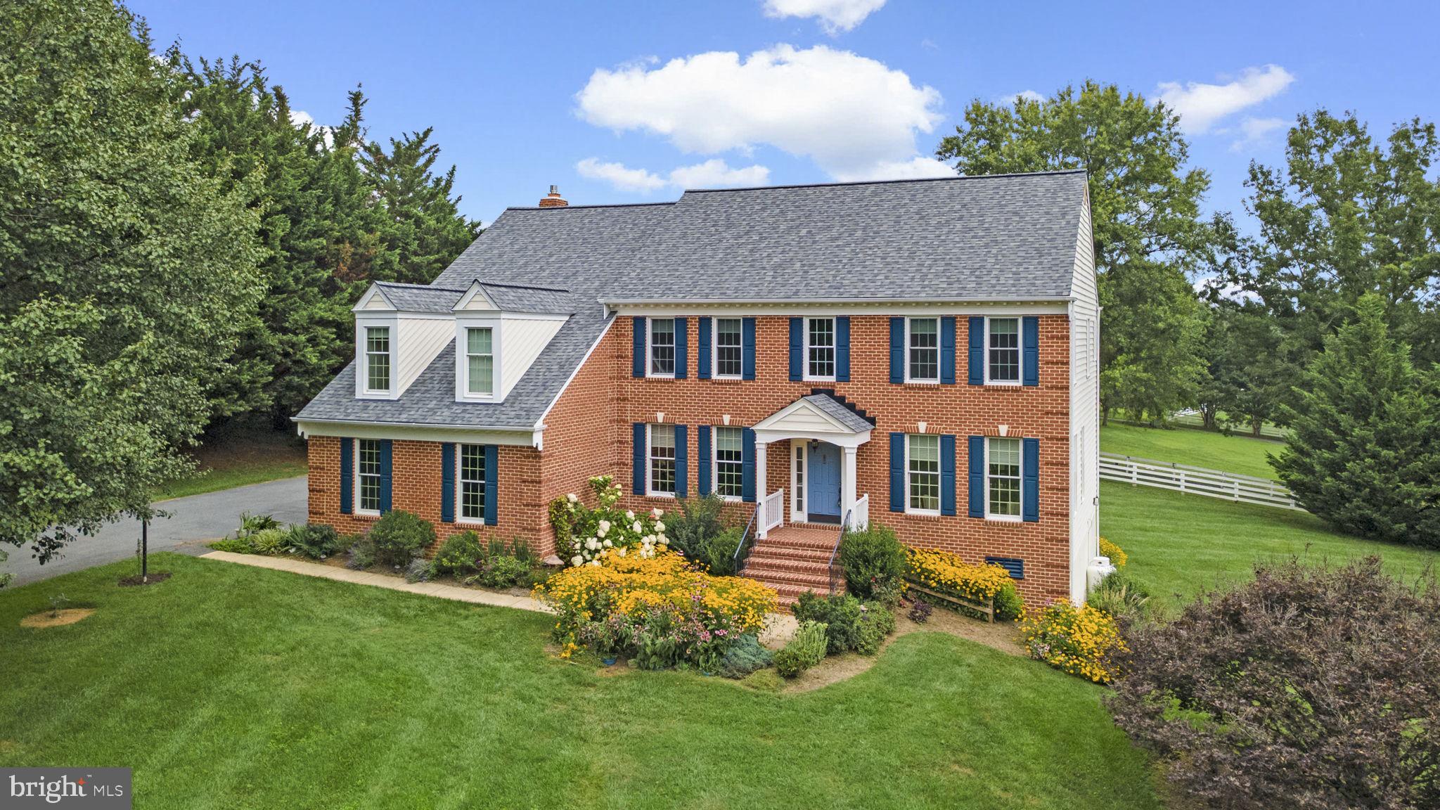 Tucked away at the end of a long, tree-lined driveway, this immaculate Colonial makes a grand first impression. An expansive front yard framed by mature trees offers both privacy and tranquility, while lush landscaping and a garden-lined pathway lead to the front entry, enhanced by a classic portico, brick façade, and vibrant blue shutters. Nestled on over two serene acres in The Paddocks, the curb appeal is nothing short of captivating.Inside, gleaming hardwood floors carry throughout the open yet traditional main level. A soaring two-story foyer introduces the home, opening to a well-appointed study on one side and a formal living room defined by elegant columns on the other. The formal dining room is accented with a chair railing and a sparkling chandelier. The stunning eat-in kitchen features luxury vinyl tile floors, a timeless white subway tile backsplash, a central island with breakfast bar seating, pendant lighting, stainless steel appliances, a pantry, and a sunlit breakfast room with direct deck access. Seamlessly connected, the expansive family room serves as the heart of the home, showcasing hardwood floors, soaring high ceilings, abundant natural light, and a dramatic floor-to-ceiling brick fireplace. A convenient powder room, laundry area, and access to the garage complete the main level.Upstairs, discover four spacious carpeted bedrooms, including the luxurious primary suite with a large walk-in closet and spa-like ensuite bath featuring a dual sink vanity, a corner soaking tub, and a glass-enclosed shower. One secondary bedroom delights with a whimsical hidden 5x8 secret room. A full hallway bath with dual sinks serves the secondary bedrooms. The walkout lower level provides endless possibilities with a generous wraparound recreation room, a versatile bonus space, and a large storage area or potential workshop.Outdoors, the deck overlooks a lush, partially fenced backyard, complete with a storage shed, a stepping-stone path leading to the front drive, and a sprawling side yard perfect for play or relaxation.