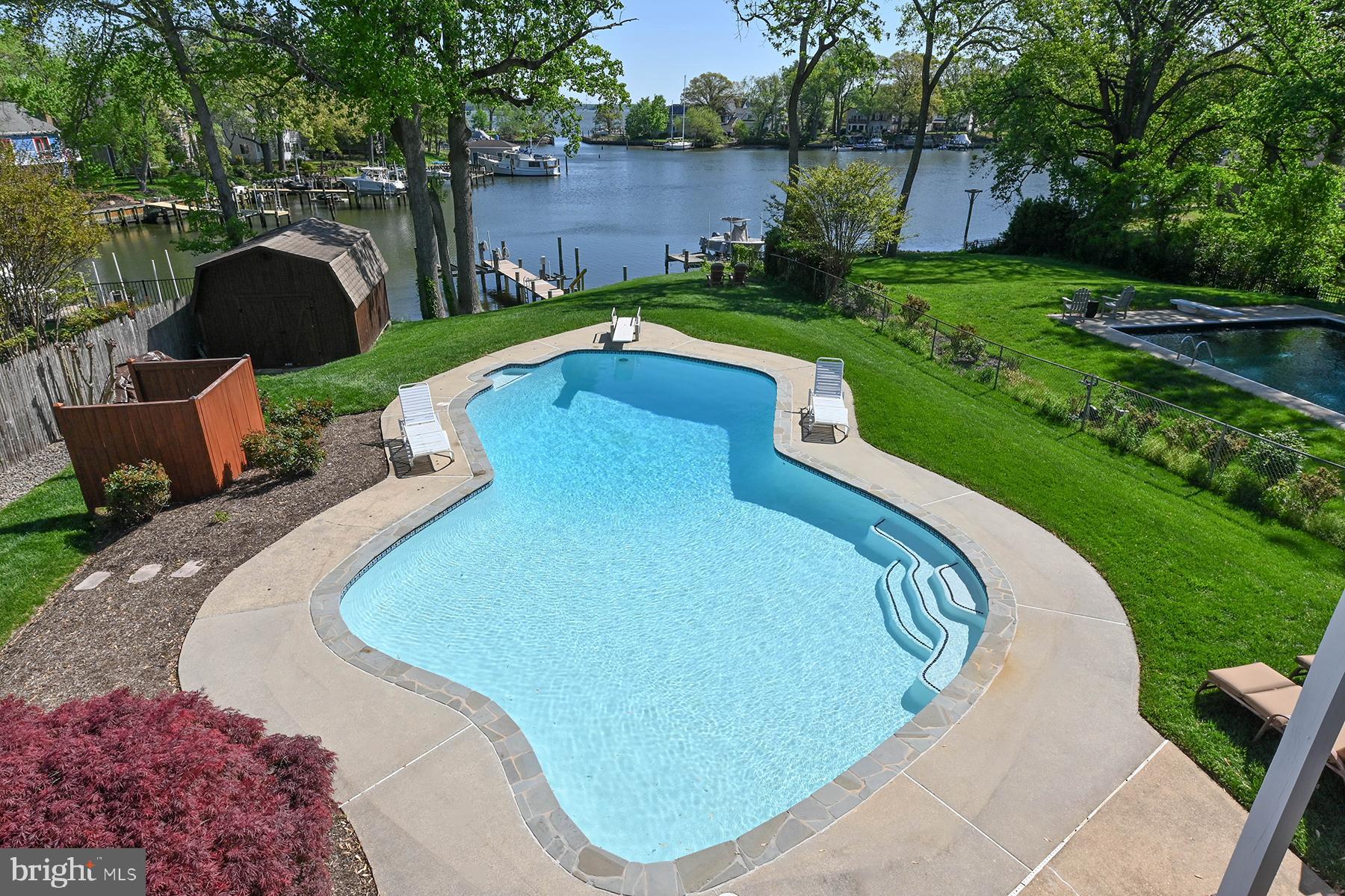 Welcome to 857 Spriggs Court, a charming waterfront home perfectly positioned along Spriggs Pond with wide-open views out to the Magothy River. This property is a rare combination of characteristics: a gentle yet elevated slope to the water, protected deep-water pier with immediate access to the river and Chesapeake Bay, and the jewel in the crown is the waterside pool that gets sun all day long. Gather with friends on the pool deck, enjoy a break from the heat under shade on the patio, or dine al fresco on the spacious upper deck — all just steps from your private pier. The pier offers a 12,500 lb boat lift and a jet ski lift. Inside, the open-concept main level is flooded with natural light and framed by sweeping water views. The seamless flow in the great room creates the perfect setting for everyday living, dining, and entertaining. The dining area features sliding glass doors that open to the large deck, and extensive built-ins featuring glass-fronted cabinets for display. The kitchen island is the perfect location for a chef who likes to be a part of the action with space for friends at the counter and connection to the other entertaining spaces both indoor and outdoor. The custom wood cabinetry is beautiful and offers ample storage, while the hardwood floors give a warmth to the whole great room. The primary suite is a peaceful retreat, complete with direct deck access, a private ensuite bathroom, and a spacious closet. The hardwood floors continue into the primary bedroom and one of the bedrooms. Two additional bedrooms and full bath complete this level. Downstairs, the walk-out lower level offers a spacious family room with a gas fireplace, direct access to the waterside patio, a full bathroom, and a separate laundry room. There's also a flexible bonus room — ideal for a home office, guest space, or workout room. The utility room offers some additional storage as does the workshop. Located in a coveted “blue ribbon” school district and just minutes from shopping, dining, and major commuter routes, this home offers an incredible waterfront lifestyle at an attractive price. Don’t miss your chance to own a private waterfront oasis with a pier on a protected cove and a waterside pool. An added benefit is watching the ospreys, herons and bald eagles dive for fish…you may even catch dinner from your pier!