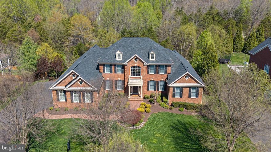 Immaculately maintained by its original owner, this turn-key Estate is perfectly situated on a quiet cul-de-sac in amenity-rich Dominion Valley Country Club. Offering over 7,100 sq ft, 5 BR / 4.5 BA, $250K+ in upgrades, 3-sided brick, and a 3-car side-load garage, this exceptional property sits on a private .77 AC wooded lot. A grand two-story foyer welcomes you with an elegant curved staircase featuring wrought iron railing. The main-level primary suite offers cathedral ceilings, a sitting room, two walk-in closets, deck access, and a mini-split heating/cooling system for personalized comfort, plus a spa-inspired primary bath. The Palladian chef’s kitchen features professional-grade JennAir appliances, highly upgraded cabinetry, and a large center island, flowing into a sunny breakfast room and the dramatic family room with cathedral ceiling and stone gas fireplace. The main level also includes an elegant formal living room, separate dining room with recessed ceiling, private home office, and gleaming hardwood floors throughout. Upstairs you’ll find a Princess Suite, two additional bedrooms with a Jack-and-Jill bath, a versatile loft, and two oversized storage closets. The finished lower level is built for entertaining with a home theater (seating and equipment convey), expansive recreation space for games and gatherings, plus Bedroom #5 with custom built-ins and a full bath. Outdoor living is equally impressive with an elegant brick walkway, extensive hardscape, a huge maintenance-free deck with built-in gas grill, patio, built-in gas fire pit with seating, and a hot tub, all overlooking the private wooded setting. Additional highlights include plantation shutters, upgraded lighting, crown molding and shadow boxes throughout, brand-new roof (2026), new upper-level HVAC, and EV charger. World-class amenities include: Arnold Palmer Signature Golf Course, renovated Clubhouse, state-of-the-art Sports Pavilion, 5 swimming pools including an indoor pool, tennis and basketball courts, playgrounds, miles of walking/biking trails and two fishing ponds. Award winning schools!