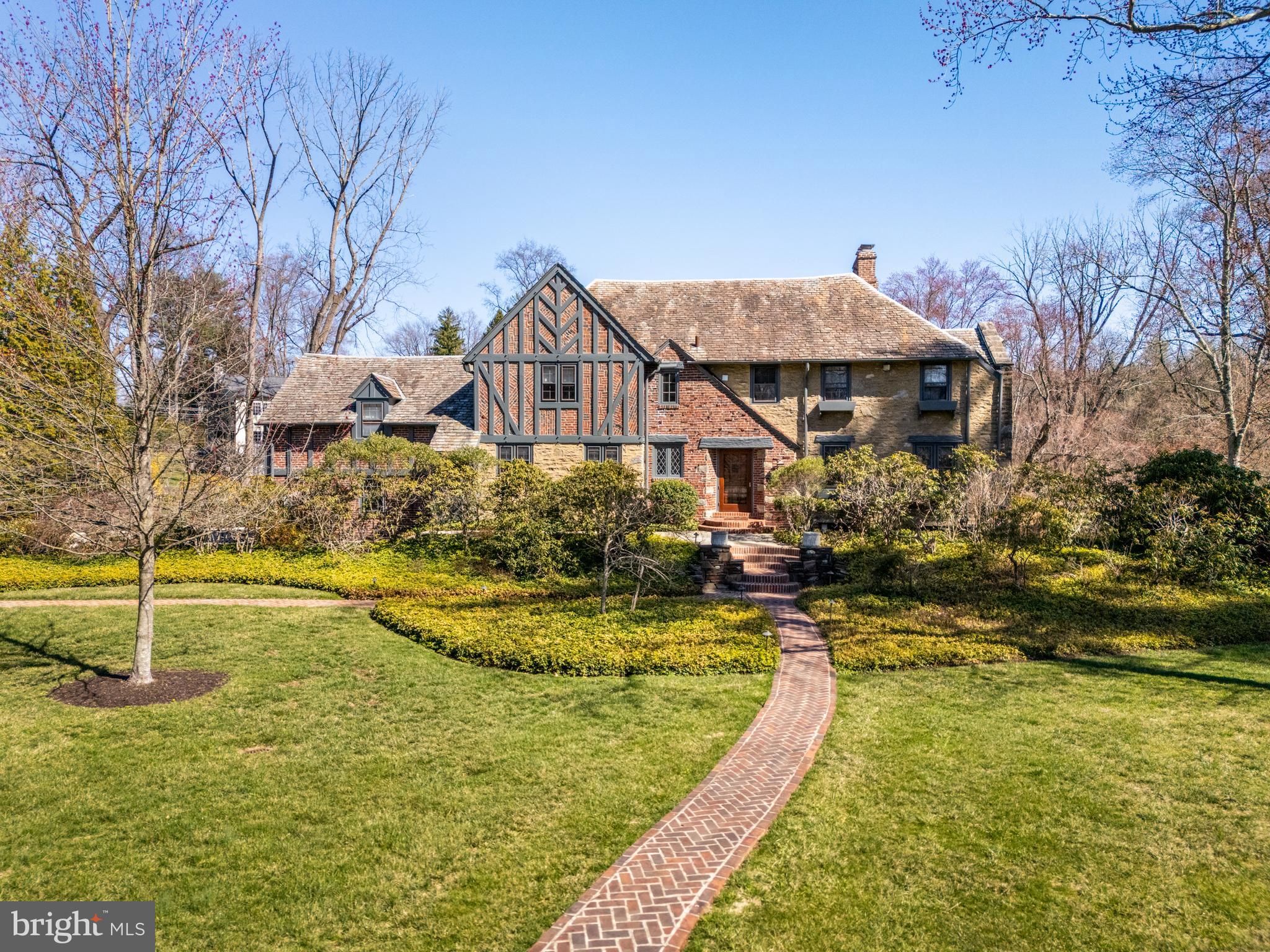 321 Airdale Road is an exquisite brick and stone traditional English Tudor situated on a beautiful .95 acre property on one of the most gracious streets on the Main Line, close to Ashbridge Park. Thoughtfully updated and expanded, this very special home includes modern conveniences as well as classic architectural finishes that give it warmth and character including a remarkable primary suite, new heating system 2020, new AC 2022 and more. The approach to the property is welcoming, with professional landscaping and a brick walkway that leads to the front door. The entrance foyer includes a half bath and coat closet and leads to an inviting private den with built in bookshelves, window seat ,and views of the property. At the other end of the foyer is the spacious eat in kitchen with 2 sub zero refrigerators, Viking 48” 6 burner range, 2 copper sinks, large center island, and plenty of storage. Through the mudroom, the back door leads to a large deck; the perfect spot to barbeque and entertain. There is also a kitchen door to the front of the house, access to the garage, and back steps to the 2nd floor and lower level. The dining room is generously sized and overlooks the amazing adjacent living room. It features a wood burning fireplace surrounded by paneling, built in shelving with lighting, and a stained glass window. This is truly a charming room. A few steps down from the dining room is the living room with soaring ceilings, incredible windows and views, wood burning fireplace, built in bookshelves, window seats, and doors leading to the side property. Steps down lead to the lower level that includes a family room with gas fireplace, wet bar, exposed beams, with steps to an outside entrance, a space that could be an office or workshop, utility room, half bath, and storage space with laundry hook up. The second floor includes a private, spacious primary suite with sophisticated finishes including custom walk in closets, dressing room, and a luxurious bath with walk through shower-a private oasis. The 2nd floor also includes 3 additional bedrooms and 2 baths (one is en suite), an office adjacent to the primary BR (could be a bedroom), a laundry and large linen closet. A walk up attic provides storage space. There is an attached 2 car garage. The property is beautifully landscaped and offers several areas to sit and relax or entertain. Close to the shops of Bryn Mawr, R5 Rosemont train station, many schools, and easy commute to center city and 476. Ashbridge Park is close by with a playground and tennis courts.