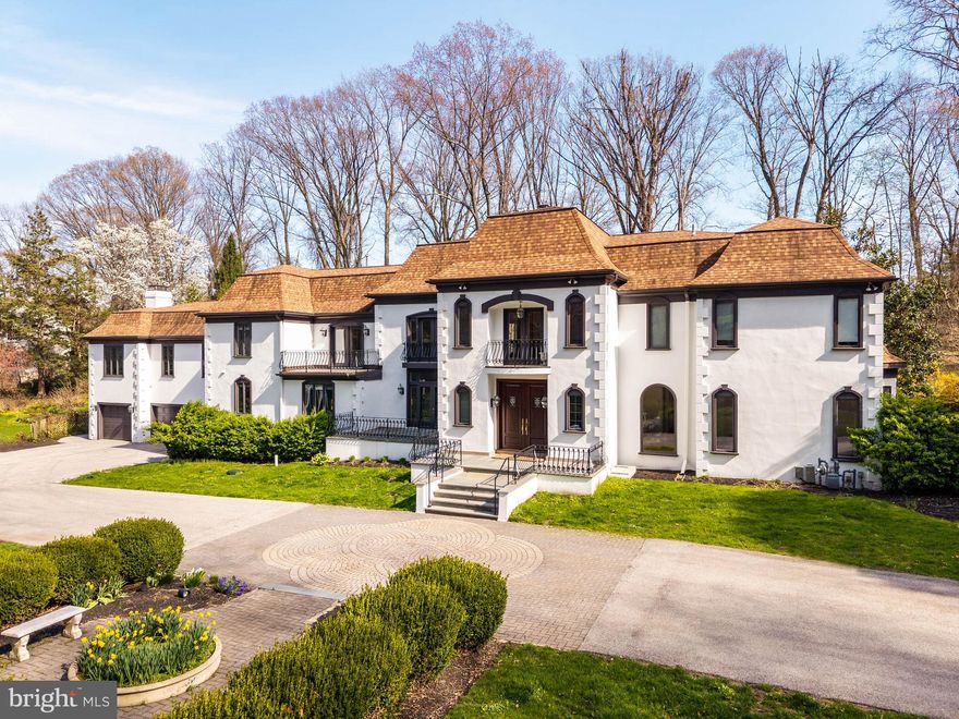 Positioned behind dual gated entrances on over 1.5 professionally landscaped acres, 1075 Green Valley Road is a French Colonial residence offering nearly 8,000 square feet of living space, extensively updated and meticulously maintained. A circular paver drive creates a strong sense of arrival, leading to double doors that open to a two-story foyer with herringbone hardwood floors and inlay, anchored by a sweeping turning staircase.

The main living spaces are defined by scale, light, and direct access to the grounds. The living room features floor-to-ceiling windows and a wood-burning fireplace, while a sitting room and dining room sit opposite, each opening through French doors to slate patios. Across the main level, the principal rooms connect seamlessly to the outdoor terraces, creating a natural extension of the living space for both everyday use and entertaining.

At the center of the home, a vaulted gathering space integrates a family room, game area, library, and office into a single, expansive environment. This space has been extensively remodeled with updated flooring, custom built-ins, a wet bar, and Murano glass chandeliers, along with modern enhancements including WiFi-controlled lighting and an integrated motorized TV lift. Direct access to the patios reinforces the connection to the surrounding grounds.

The kitchen is both functional and inviting, with custom cabinetry, granite countertops and backsplash, stainless steel appliances, and a fireside dining area. Skylights and surrounding windows provide consistent natural light, while the adjacent enclosed porch with a built-in grill extends the space for year-round use.

Upstairs, the primary suite includes a fireplace, a spacious bath with soaking tub, glass-enclosed shower, built-in vanities, and an oversized dressing room with custom built-ins. Additional bedrooms are well-proportioned with access to updated baths, including a spa-inspired bath featuring a wet room, freestanding tub, dual showers, and custom finishes.

The fully finished lower level adds another layer of functionality, featuring additional living space, fitness area, full bath, and sauna—well-suited for guests, recreation, or private retreat.

The outdoor setting is defined by multiple slate patios, mature landscaping, and a lagoon-style swimming pool with integrated spa, creating a resort-like environment.

Extensive mechanical and infrastructure upgrades have been completed, including new heating and air conditioning systems, comprehensive insulation improvements, LED lighting throughout, WiFi-enabled thermostats, and a repaired septic system. Exterior improvements include full stucco remediation and painting, upgraded irrigation with WiFi control, enhanced gated entry systems with video and remote access, and new pool equipment.

Located in Lower Merion Township with convenient access to Route 30 and I-76, and within close proximity to the Main Line’s schools, clubs, and dining, 1075 Green Valley Road offers a rare combination of scale, setting, and meaningful upgrades, aligned with the expectations of today’s buyer.