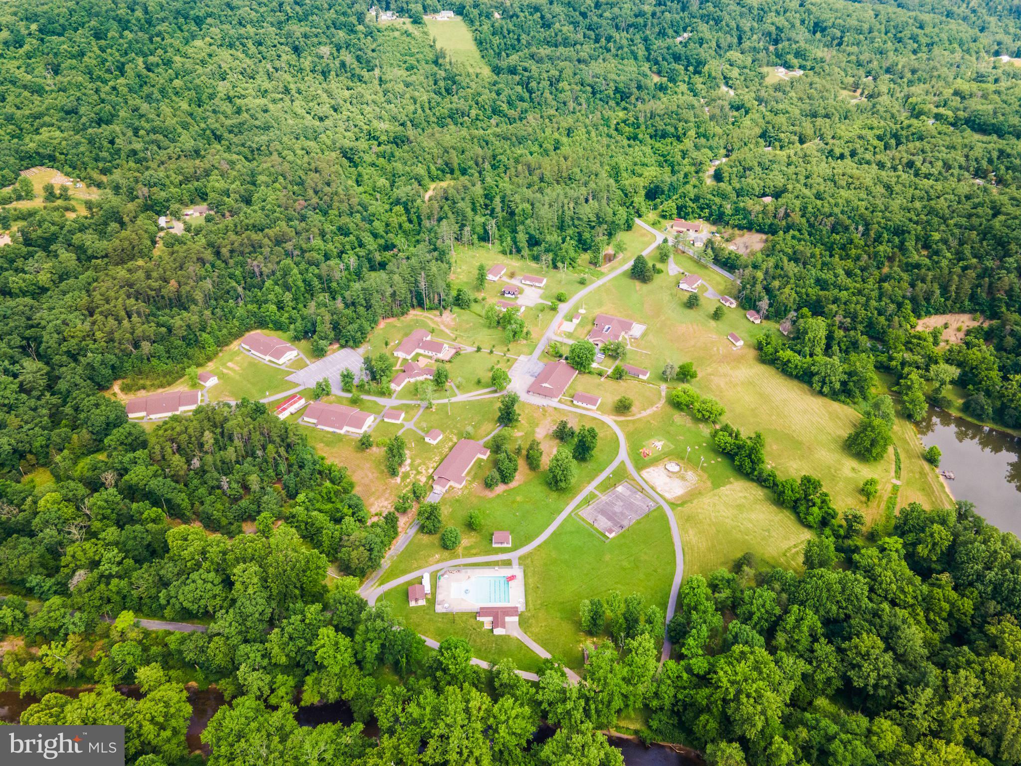 An amazing property being offered for sale on behalf of an international non-profit organization! Welcome to Camp Tomahawk, a complete, modern retreat center and campground in the beautiful pastoral mountains of West Virginia. This turnkey, fully operational campground offers everything from high-tech conference and chapel buildings to commercial-grade kitchen, dining, meeting, classroom, and recreational facilities for up to 300 guests. There are three fully-furnished, comfortable homes for company directors and officials to live in with their families while at the property. The main conference building itself offers hotel-style rooms for twenty guests, while two additional buildings provide plenty of room for staff housing. There are three large bunkhouses for campers and counselors, plus a camp caretaker’s residence. The property is 168 deeded acres and the camp is certified by the American Camp Association (ACA). Recreational amenities include an event barn for program activities, a swimming pool, a campfire ring with bleacher seating, a pond for fishing and boating, a mountaintop observation tower, several picnic pavilions, two ropes courses, and numerous sports fields and outdoor activity stations. This secluded retreat is well suited for a variety of corporate, private, and charitable uses, including hosting leadership meetings and staff teambuilding adventures. It has been serving for 40+ years as a youth campground and is well known and loved by the surrounding communities. The property is located only 15 minutes from Interstate 81 and Martinsburg, WV and about 30 minutes’ drive from Winchester, VA, Hagerstown, MD, and Charles Town, WV. Guests will feel their stress melt away as they drive the scenic country roads leading to the camp, leaving behind the crowds and congestion of the daily grind. When they arrive and turn in through the gates, they’ve found an opportunity to relax and recharge.