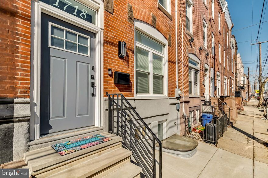 Welcome to 1718 S 18th Street — a stunning custom renovation located in the highly desirable Newbold section of South Philadelphia, offering valuable tax abatement savings and exceptional modern finishes throughout. This extra-wide, three-story residence features 3 bedrooms and 3.5 bathrooms, including two en-suite bedrooms. The home blends thoughtful design with everyday functionality, highlighted by soaring ceilings, wide-plank solid oak flooring, and abundant natural light. The main level features an open-concept layout ideal for entertaining, with a convenient powder room, a statement wall, and a generous pantry/closet space. The beautifully appointed kitchen features ample cabinetry and storage and flows seamlessly into a spacious rear yard finished with a new concrete patio — perfect for outdoor dining and entertaining. The second level boasts a custom wet bar designed for effortless hosting. Two spacious bedrooms with two well-appointed full baths and a convenient laundry.  The upper level features the primary suite, with an oversized shower and double-sink vanity, creating a spa-like retreat. The floor also gives direct access to a bi-level Trex roof deck. A spiral staircase leads to the upper deck, offering breathtaking 360-degree views of the Philadelphia skyline. The durable Trex decking ensures long-lasting, low-maintenance outdoor living. Additional features include abundant closet space, two washer/dryer hookups (second floor and finished basement), two-zone high-efficiency gas heat and central air, smart thermostats, and a Simplisafe security system. The fully finished basement is a fantastic flex space and has been professionally waterproofed, with a French drain system and egress, providing peace of mind and flexible additional living space. Conveniently located near the Broad Street Line at Tasker-Morris Station, offering easy access to Center City. Enjoy close proximity to neighborhood favorites, including Ultimo Coffee, South Philly Tap Room, Second District Brewing, American Sardine Bar, Hardena, Batter & Crumbs, Two Eagles Cafe, and The Tasty Toast, along with all that East Passyunk and South Philadelphia have to offer. This home epitomizes modern city living with space, style, and convenience in one of Philadelphia’s most sought-after neighborhoods.