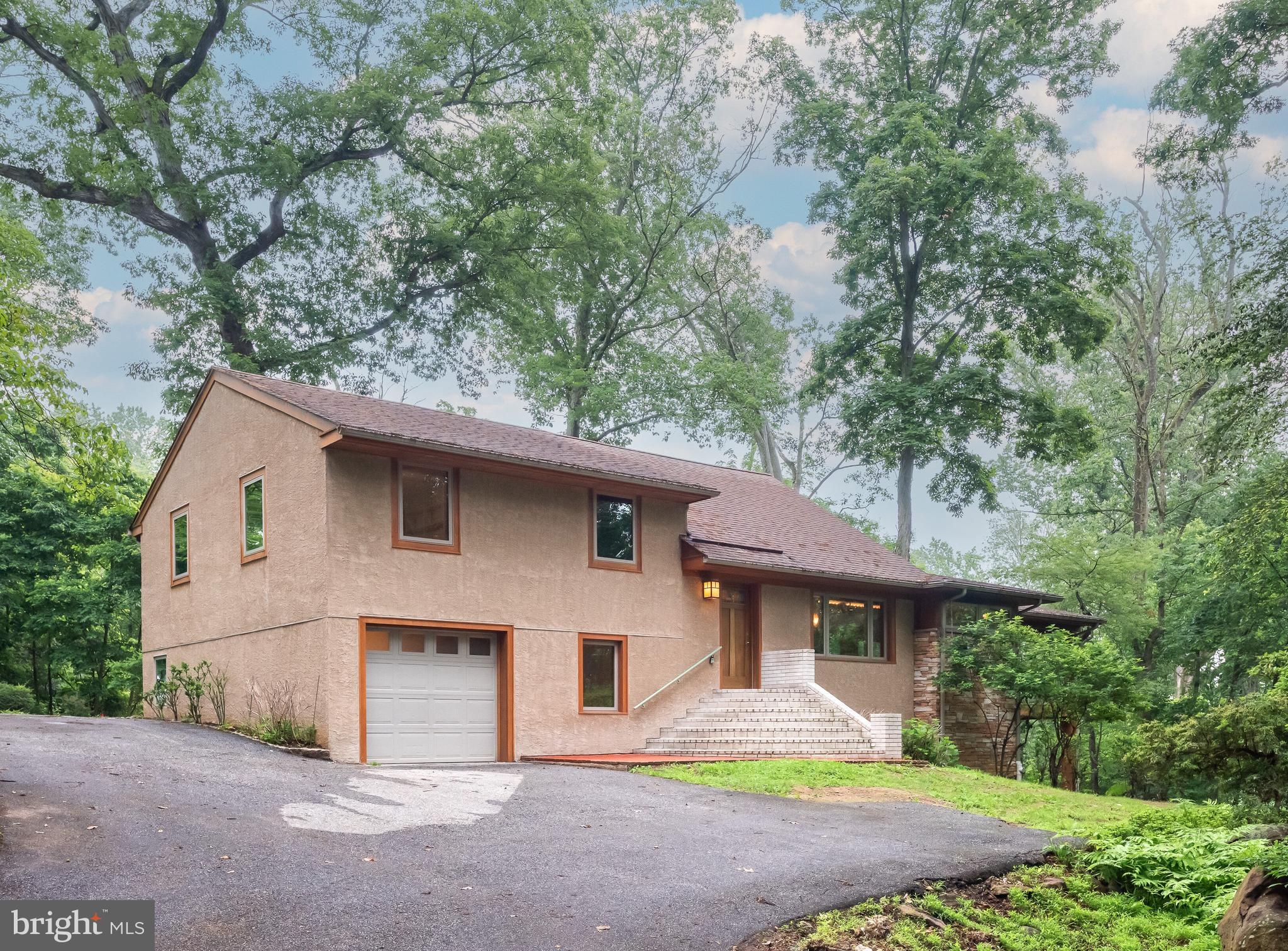Welcome to 54 Grist Mill Road, a beautiful and unique home nestled in Thornbury Township in Glen Mills and within the award-winning West Chester Area School District.This amazing 4-bedroom, 2.2 half-bath home offers comfort, flexibility and functionality in a serene, wooded setting. Step inside to a charming foyer with elegant archways that draw you into the heart of the home. The thoughtfully designed kitchen showcases newly installed stainless steel appliances with a beverage cooler and includes a built-in refrigerator that blends seamlessly with the cabinetry. Just beyond, the spacious Great Room features soaring ceilings with gorgeous custom lighting, hardwood floors, a striking central fireplace, and expansive windows that flood the space with natural light. Step out onto the covered back deck, ideal for enjoying peaceful mornings with a cup of coffee or hosting gatherings with effortless indoor-outdoor flow. You will also find a conveniently located powder room on the main level.
The Great Room also features a beautifully lighted, spiral staircase leading to a spectacular space on one of the lower levels. This room was designed as an artist’s studio, with its own AC, heated floors, a wet bar and a kiln room; but using your own imagination and depending upon your needs, it could be an additional family room, or an in-home gym and spa area, with plenty of room for a hot tub and sauna! AMAZING SPACE!! Leading down a few steps from the kitchen there are 2 lower levels. On the first, you will find a perfect in-home office and/or library space with hardwood parquet flooring, as well as the laundry room and the 2nd half bath. Then there is the huge unfinished basement with tons of storage space, the whole-house vacuum and lots of room for a workshop. Upstairs, you’ll find three generously sized bedrooms and a full bath on the second level, while the third level is dedicated to the primary suite with its own bath and walk-in closet. Architect-designed and remodeled in 2005, the home features passive solar elements that enhance both energy efficiency and year-round comfort. A whole-house generator provides uninterrupted power, offering peace of mind during storms—especially beneficial for those who work from home. The seller has spared no expense in preparing this home for you, including the installation of a totally new septic system, as well as freshly painting the entire home and refinishing the hardwood floors on the upper and lower levels. You are surrounded by nature and spectacular wooded views on every level of this amazing home, while still being just minutes from top-rated schools, popular shops, dining, and major routes for commuting. 54 Grist Mill Road is a rare blend of beauty, charm, seclusion, convenience, and modern living—schedule your showing today!