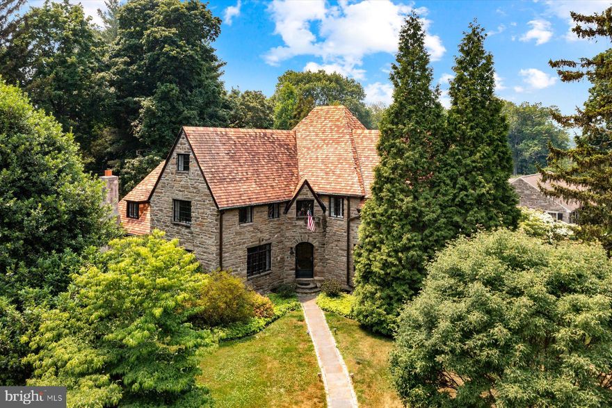 In a tucked away corner of Chestnut Hill, this c. 1929 French Normandy residence showcases beautifully proportioned rooms and a wealth of updates. A central foyer, large enough to accommodate the bar for your next soiree, is the central point from which all the major rooms spoke off. A grand-scale formal living room with wood-burning fireplace and beamed ceiling accommodates multiple seating areas. This space features plenty of natural light with casement windows and a set of French doors that open to a Juliette balcony. A very comfortably sized formal dining room, awash in natural light, seats a crowd with ease. Like many homes of this era, the butler’s pantry and kitchen are adjacent to the dining room, and the kitchen also is accessible from the foyer. The kitchen features neutral finishes, a tile backsplash, a broad window over the sink and stainless appliances, including an extra wall oven to supplement a gas range. Step down to a library/study with a gas fireplace and wall of built-ins. Again, the scale of this space is such that it accommodates multiple activity areas. All of the main rooms, along with the staircase from the first to the third floors, have gleaming, refinished wood floors. A large patio, ready for summer entertaining, is accessible from the butler’s pantry. Private quarters on the second and third floors include a large owner’s suite with tile bath, sitting area and dual closets behind French doors. An adjacent room can be a second bedroom or separate sitting room for the owner’s suite. This room, along with another, very expansive bedroom, accesses a gorgeous new full bath finished in marble. An au pair or guest suite with full bath is accessible from this room as is a rear staircase. The third floor has three bedrooms and a full hall bath. With electric upgraded, newer air conditioning units, newer security system, updates to the garage and fresh paint throughout nearly every room, plus other updates, this residence is move-in ready. A fenced yard is ready for dogs and kids to play. A wonderful opportunity to own in Chestnut Hill, just steps from the Morris Arboretum.