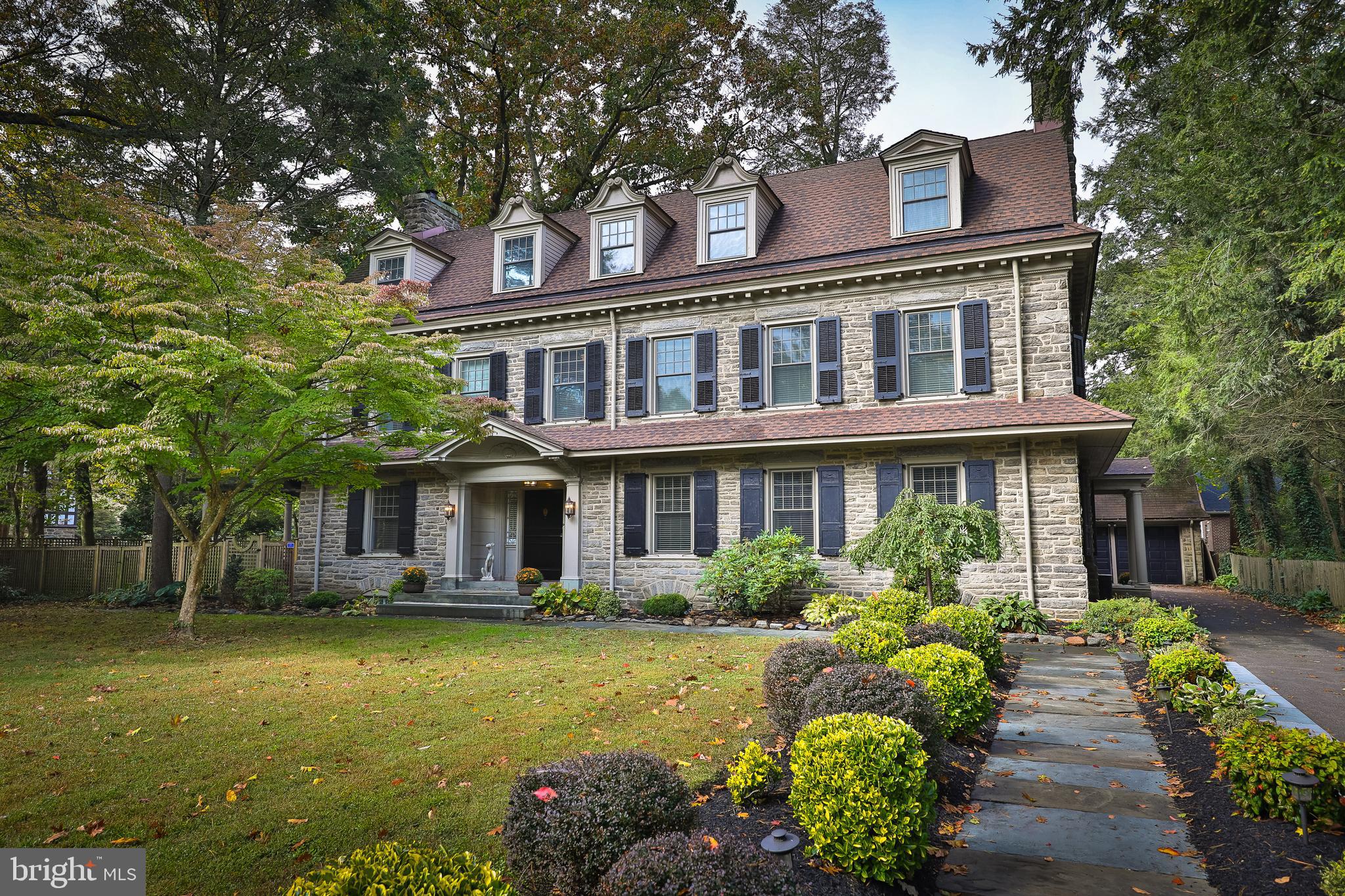 If current events have you seeking a home that can provide a sense of peace and calm, plentiful outdoor space, and ample room for multiple offices, then look no further. Designed in 1912 by George T. Pearson, this exquisite stone colonial is throughly updated for today's discerning buyer and exudes warmth and comfort. Upon entering you will be struck by the casual elegance of the detailed woodwork, lovely archways and grand staircase with arched window on the landing. The living room has a large fireplace flanked by two sets of French doors leading to the side patio and pergola, a perfect flow for entertaining and for indoor/outdoor living. Host friends and family for dinner in the large dining room, which features a second fireplace, beautiful built-in cabinetry, and a custom-built sideboard. The kitchen has been fully renovated with stunning, leathered granite countertops, Wolfe range, and large farmhouse sink. The large island provides seating and storage and well as built-in Bosch dishwasher. Exposed brick and stone add a rustic yet contemporary feel, while the butler's pantry with double sink and original tin countertop are a nod to the original design. A wine cellar sits below the kitchen floor. The kitchen opens to a bar/sitting area with exposed beams, skylight and renovated half bathroom. Upstairs you will find the two-room primary suite comprised of a lovely bedroom and a large sitting room, which could easily serve as another bedroom. Stunning primary bathroom features heated floor, beautifully tiled shower with multiple shower heads, double vanity with marble surfaces. From the bathroom or from the hallway you will enter a full custom dressing room complete with built in shelving, a marble-topped island with drawers. Also on this level are an office with plenty of built-in storage, a laundry room large enough to be nursery or small bedroom, and another full bathroom. The third floor offers even more flexibility. Two bedrooms and renovated hall bath with clawfoot tub/shower form one wing, perfect for guests. The remaining wing features a third bedroom or office, a smaller unheated room perfect for crafts, yoga or storage, and a very large bonus space with gorgeous bathroom. This space is currently used a a home gym but would make a lovely primary bedroom, playroom, etc. Current owners have made numerous upgrades, including four and half newly renovated bathrooms, each with tasteful tile, marble vanities and high end finishes, fully renovated kitchen and bar, A/C added to 2nd and 3rd floors, 22 new windows, two new plumbing stacks, new boiler in 2018, new hot water heater in 2015, and much more. Situated on just over .5 acres of beautifully landscaped land, you will find plenty of opportunities to spend more time outdoors. Gather with friends and family around the stone fire pit under the newly built pergola, plant vegetables in the raised garden beds, play in the large yard, or relax in one of the many secluded corners. The detached two-car garage has unfinished space above perfect for a studio. The house and grounds are so lovely you may never want to leave but when you do, you will love being in the heart of popular West Mount Airy. It is an easy walk to Carpenters Woods, the trails of the Wissahickon, High Point Cafe, Blue Marble Books and Weavers Way. This is a truly exceptional property in a coveted location, don't miss your chance to see it!