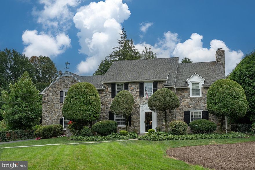 This beautiful, elegant, classic stone colonial is located on a quiet street in the heart of Bala Cynwyd. As you walk to the home you are immediately impressed by its noteworthy stature & many charming architectural details. The sun-filled home is ideal for  gatherings & entertaining with a wonderful flow from the center hall. There are hardwood floors throughout the 1st & 2nd floors. 
The main entrance has a center hall with a coat closet & nearby powder room. To the right is a substantially sized living room anchored by a large wood burning fireplace with a wood & brick surround and beautiful mantel. Many large windows invite natural light to steam throughout the home. A half-light door leads to a covered patio overlooking a stunning backyard. 
From the center hall double french doors open to a formal dining room that features a large bay window overlooking the backyard, built-in corner cabinets, wainscoting, privacy door to the kitchen, and single half-light door to the rear covered patio.
The kitchen has random width  hardwood floors, custom wood cabinetry, tile back splash, center island with seating &  a cook top. Additionally there is a corner mini station with glass cabinets, a bar sink, plus a separate breakfast area with a ceiling fan. You can access the 2nd floor and the basement from a set of backstairs, one to the 2nd floor and the other to the basement laundry room. The kitchen also has a back door that accesses the backyard, driveway and the garage. 
A small study is located off the center hall. The study has knotty pine walls, built-in cabinets, bookshelves & hardwood floors. This is a perfect room for a home office or cozy den. 
An attached garage is accessible from the rear driveway or from the charming front terrace & breezeway. 
The main stairway turns at a mid-level landing & elegantly leads up to the 2nd floor with a wrap-around banister. At the top of the stairs is a large landing and a built-in glass curio cabinet to display all your favorite collectables. The 2nd floor features 6 bedrooms & 4 full bathrooms. Bedrooms 5 and 6 can also be accessed from the backstairs. 
The Primary bedroom is lovely & spacious with 3 closets including a large walk-in closet. The ensuite bathroom has a stall shower. Bedroom 2 is large and features a private ensuite bathroom with a tub/shower. Bedrooms 3 & 4 are also quite sizable and share a hall bathroom. Additionally, bedroom 3 has a door to a roof deck and a beautiful wall of built-ins with glass doors. Bedroom 4 is also a spacious size & shares the hall bathroom. The hall bathroom features a stall shower. A large cedar closet, linen closet, and Bessler stairs to the attic are all located in this hallway. Bedrooms 5 & 6 are accessible through the private back stairs from the kitchen or from bedroom 4. They are smaller and share a full bathroom with shower/tub.
At the top of the backstairs is a private landing with a hallway that has built-in bookshelves and  sunny window seat. This is not just any window seat; this has storage plus a hidden laundry chute that goes directly to the laundry area in the basement.
The full basement is mostly finished & features a wonderful recreational space that has knotty pine walls with built-in seats & a convenient dry bar. This is the perfect party room or family room with extra space that could also host a home gym. The basement also has separate rooms for the laundry , utilities and a quarter bathroom (just a toilet). The basement is accessible from the stairway in the center hall as well as from the back stairway in the kitchen.
Truly special features of this home are the grounds. Enjoy the beautiful perimeter landscaping & large level private backyard. It is rare to find a home with this classic beauty & elegant craftsmanship on a private half-acre in this most desirable area. The property is a short walk to the Cynwyd Heritage Trail, the Cynwyd Commuter Train , #44 bus to CC. ,as well as Cynwyd Elem School and BC Middle School..