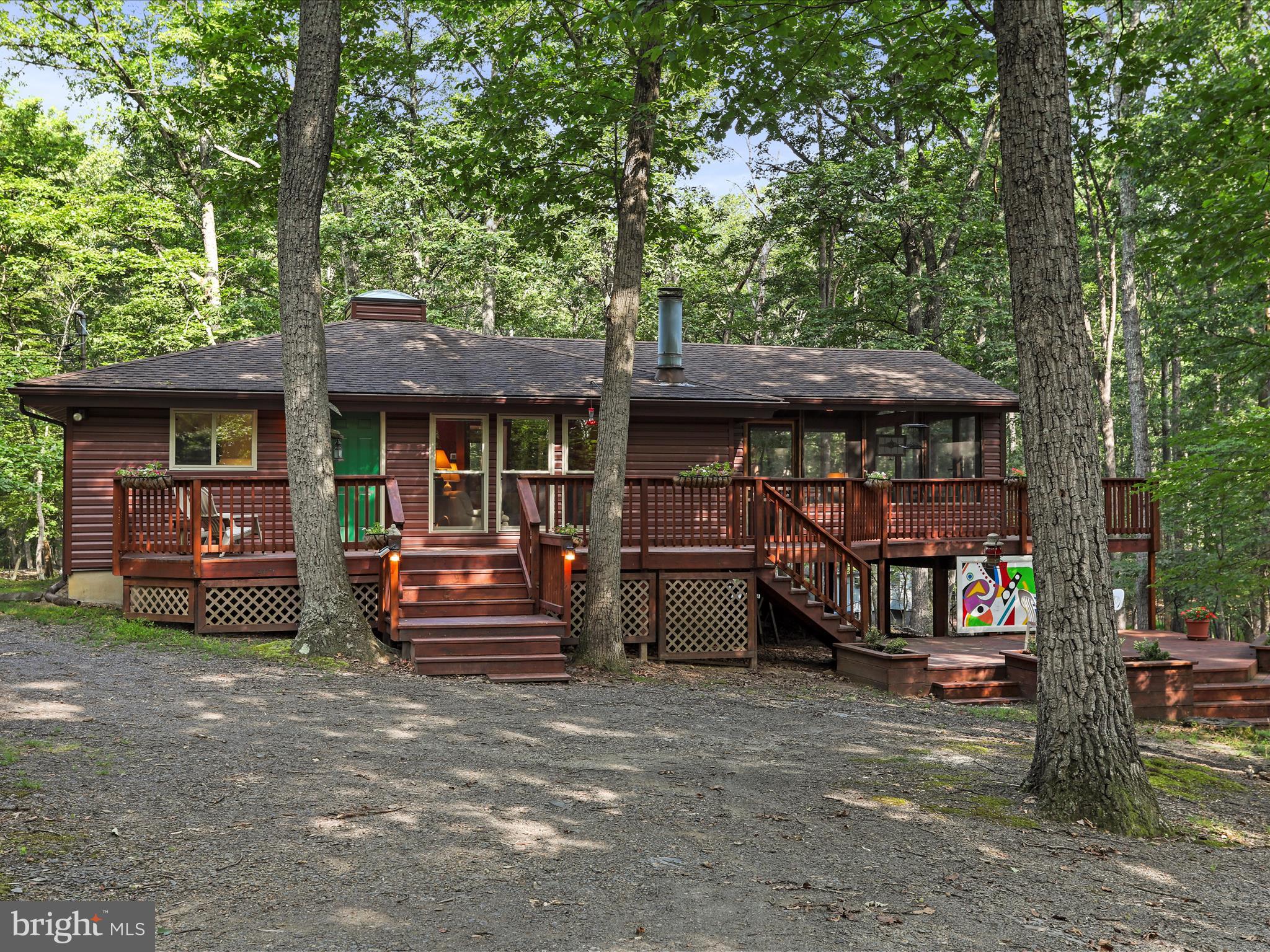 Artful Escape on Mild Winter Road
127 Mild Winter Rd | $379,900 | 3BR | 2BA | 1,024 Sq Ft | Class A Membership Included
Nestled beneath a canopy of mature hardwoods, this inspired mountain retreat blends rustic charm with artistic spirit—a home that feels both carefully curated and effortlessly livable.
Set on a beautifully wooded lot, the property underwent a thoughtful transformation just three years ago:
- New HVAC system for year-round comfort
- New windows, and sliding door to invite light and forest views
- New log-style siding, accented by a new welcoming front door
- Interior repainting throughout for a fresh, cohesive backdrop
- A rebuilt deck system and 18x18 screened-in porch that embrace the outdoors with intention
Step inside to a beautifully remodeled kitchen where quartz countertops, stainless steel appliances, and luxury vinyl plank flooring meet style and utility. Over the counter, remote-controlled pendant lighting shifts colors with the tap of a button—casting a warm glow for everyday meals or setting the mood for evening gatherings.
The open-concept living and dining space is anchored by a wood-burning fireplace, framed by a soaring vaulted ceiling adorned with two 8-foot original art panels, created by the seller and offered as part of the home’s unique character.
Plush carpeting carries throughout the bedrooms and living spaces, adding comfort underfoot and reinforcing the home’s easy, relaxed rhythm.
The primary suite features a vaulted ceiling, a thoughtfully placed awning window ideal for bed placement, and a four-piece bath with an added window to invite natural light. Two guest bedrooms—each with vaulted ceilings—share a second full bath, creating a balanced and functional layout.
Outdoor living is as inspired as the interior. A ground-level deck offers space for dining, lounging, or quiet evenings around a firepit. As a backdrop, a custom outdoor art piece, also created by the seller, will convey—an artistic exhale in a serene woodland setting.
Furniture can convey at no cost, excluding select antique pieces, art, and personal items.
A Class A Membership to The Woods Club is available, providing access to golf, indoor/outdoor pools, tennis, fitness facilities, and more. The one-time initiation fee is $3,150, and annual dues are $2,600.