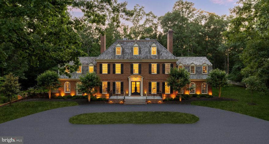 Manor Stone Drive is arguably one of the Capital Region’s best-kept secrets. Nestled along a wonderfully tranquil stretch of River Road adjacent to the Bretton Woods Club, it is a picturesque enclave of estate homes set deep into large wooded lots. 13300 is one of such homes, surrounded by white picket fences and mature foliage on five acres of land. With gardens designed by D.A. Dunlevy, the grounds, introduced by automatic gates, are a whimsical blend of sweeping vistas and towering trees. Originally constructed by master builder Patrick Cullinane, the property’s complete transformation is an homage to his exacting attention to detail and uncompromising penchant for quality. Its classically symmetrical, handmade red brick and restored wooden facade is a natural complement to the verdant backdrop. An expanded architectural front porch, featuring custom brass railings, creates a formidable first impression revealing a traditional center hall floor plan. The original wide plank hardwood floors have been restained to an elegant black, complementing intricate millwork which Cullinane’s artisans hand carved in each of his homes. Every aspect of the home is equally adept at hosting lavish gatherings as they are intimate daily life, from the formal dining room with its picture frame molding and roaring fireplace to the formal living room accessed through the builder’s famous archways to the cozy family room with its coffered ceiling and arched windows. Off the formal living room, a refined covered patio with marble floors, brick archways, recessed lighting, and designer chandeliers offers an elegant indoor-outdoor flow—perfect for seasonal entertaining or relaxing with lawn views. The highlight of the main level is arguably the soaring double-height library with spiral staircase, grand fireplace, and custom built-ins. Another is the show stopping Jack Rosen kitchen, whose exotic slabs of Brazilian quartzite are a feast for the eye alongside inset cabinetry and a hidden Thermador appliance package. The primary suite is noteworthy for its dual custom walk-in closets and sumptuous bath clad in contrasting black and white marble with heated floors, evoking images of the finest hotel suites, globally. It overlooks the rear of the home and features a private terrace, wood burning fireplace, and custom California Closets. Such premium touches throughout as Restoration Hardware fixtures, Emtek hardware, and custom Trustile interior doors are a testament to the no-expense-spared mentality when transforming the home. On the two upper levels, the five secondary bedrooms each have a luxurious ensuite bath and share conveniently located laundry facilities as well as a large open terrace overlooking the expansive lawn. The lower level, with its high ceilings, is an entertainment hub. Its floor plan revolves around a large recreation space, branching off into a fitness center with rubber flooring and accompanying full bath. The true professional home cinema is capped by a showstopping starlight ceiling similar to what is found in Rolls-Royce automobiles, and features state-of-the-art 4K projection and Dolby Atmos surround sound equipment. Systems upgrades include a smart energy management suite, intelligent HVAC, electric blinds, improved interior lighting, fully-redone plumbing and water treatment, and low voltage LED lighting around the property to create a radiant glow after the sun sets. Surrounded by five acres of flat, usable, green natural beauty, 13300 Manor Stone Drive is an elevated country estate providing a serene escape from the hustle of urban living.