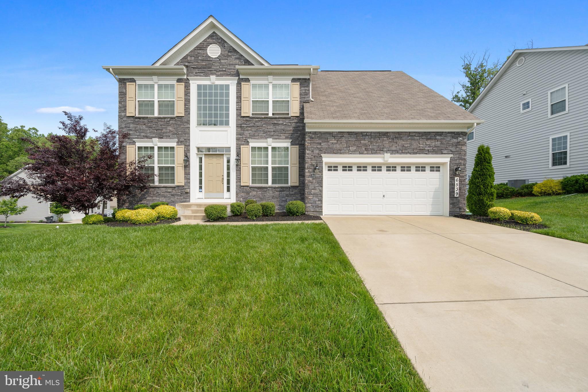This 6-bedroom home with a finished basement in Windsor Manor sits on a coveted corner lot and has outstanding curb appeal. The house has a gorgeous stone facade, while the front of the property includes a lush lawn with a sprinkler system, and landscaped planting beds lining the walkway to the front door.
Inside, you’ll find luxury vinyl plank flooring throughout, plus high ceilings, custom millwork and oversized windows that fill the space with natural light. Just off the foyer, there’s a formal dining room on one side and a den on the other.
At the back of the floorplan, the kitchen includes recessed lights, granite countertops, stainless appliances, a pantry, a center island and a breakfast bar overlooking the morning room with vaulted ceilings! The large adjacent great room includes a stunning stone fireplace. The main level also offers a bedroom/flex room and full bathroom, perfect for in-laws or your home office.
Head upstairs to find four bedrooms and the all-important second-floor laundry room. All the bedrooms have ceiling fans, and the primary boasts tray ceilings and a custom walk-in closet. The primary ensuite offers his & her vanities, a center soaking tub and a unique walk-thru shower with dual shower heads.
Still need more space? This 3,300 sq ft home includes a completely finished basement, which has a bedroom, full bathroom, storage space, a game/rec room with a wet bar and a home theater (with surround sound+screen+elevated platform). The rec room also has a slider that walks out to the backyard.
Windsor-Manor is a quiet subdivision close to the Potomac River, it has walking paths and a playground You’ll also be close to schools and lots of shopping options along 210/Indian Head Hwy. and just minutes to National Harbor and D.C.!