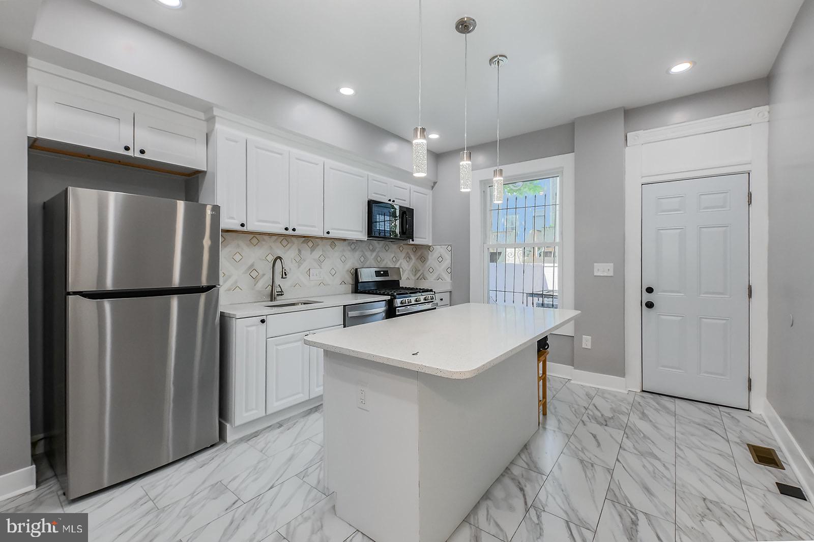 Step inside this beautifully renovated townhome and discover a space that’s both functional and thoughtfully designed. The entry opens into a cozy vestibule that flows right into a spacious, open-concept living area—perfect for relaxing or hosting. The kitchen is updated with granite countertops, stainless steel appliances, a gas stove, pendant lighting, and a knee bar fit for stool seating that creates a natural connection to the living space. Upstairs, you’ll find two well-sized bedrooms with great natural light, plus a middle bonus room that could serve as a home office, nursery, or guest space. The full bathroom on this level features modern tile and clean, contemporary finishes. Downstairs, the lower level offers a third bedroom with recessed lighting and carpeting, a second full bath with stylish tilework and updated fixtures, and a convenient laundry area with washer and dryer. Out back, the fully cemented yard with tall privacy fencing makes for a low-maintenance retreat—ideal for outdoor dining, string lights, and quiet evenings with friends or family. Located in close proximity to Johns Hopkins, public transit, and major roadways, this home offers a great blend of city access and neighborhood feel. Whether you’re looking to settle in or invest, this home has the setup and style to make it a smart move. Don't miss your chance to see this home in person. Schedule your tour today.