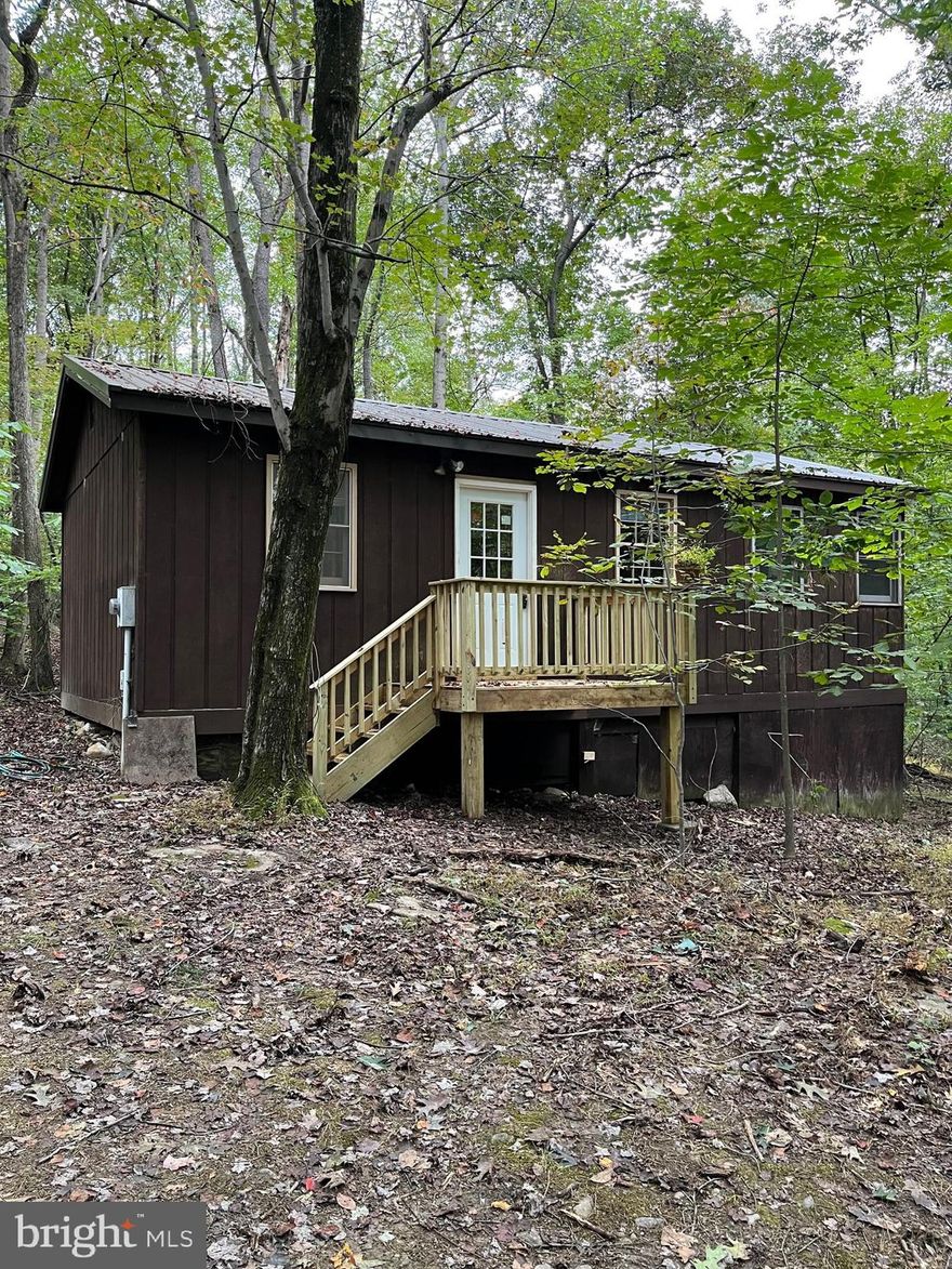 2BR, 1BA cabin in Cacapon River Meadows.  Situated on 2 wooded acres, this cabin is tucked back in the trees for privacy.  Living Room, Dining, Kitchen combo, along with 2 bedrooms and 1 Bath.  New Deck was installed 9/2022.  New Metal Roof was installed 7/2021.  Community owns a river front lot on the Cacapon River for easy access to swim, canoe or fish.  Adjoining 2.54 Acre lot available and being sold separately. Weekend getaway at an affordable price.  Being sold as is.