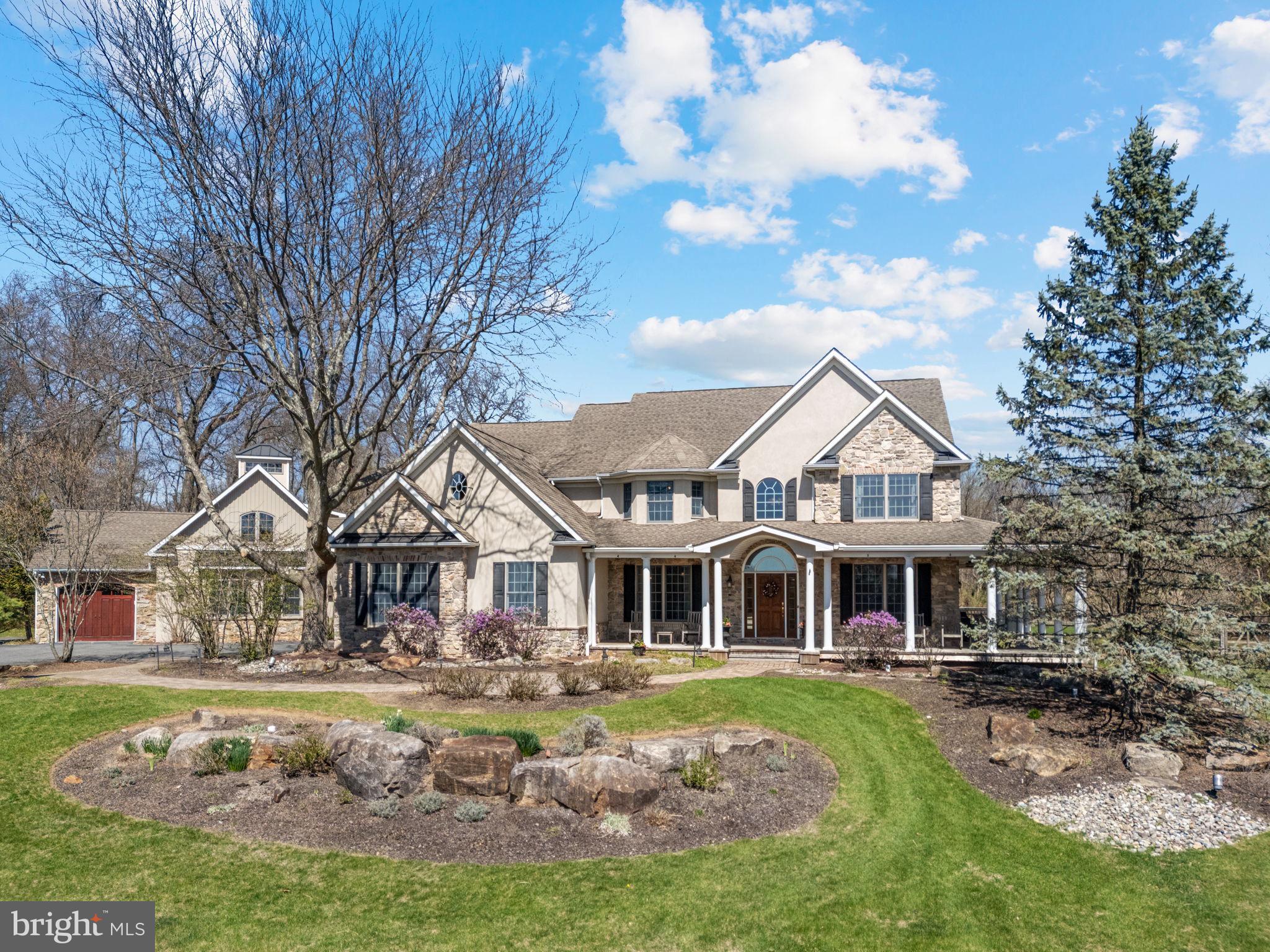 Set on 3.26 beautifully landscaped acres in Lower Saucon, this custom-built home offers over 5,400 square feet of refined living space, including a private 2-bedroom in-law/guest suite. The covered wraparound porch with cedar flooring sets the tone for the craftsmanship and attention to detail found throughout the home. Inside, Brazilian cherry floors and soaring ceilings elevate the interior. The kitchen is designed for serious cooking and entertaining, featuring cherry cabinetry, granite counters, a separate wet bar, and ample prep space. The adjacent breakfast room, with vaulted ceilings and panoramic backyard views adds charm and natural light. The family room is anchored by a dramatic floor-to-ceiling wood-burning fireplace. Separate formal living and dining rooms, along with a private home office, offer versatility for both entertaining and everyday function. A custom mudroom with built-in storage leads to a spacious laundry room with plenty of cabinetry and a tiled dog wash. Upstairs, the primary suite is a private retreat with a sitting area, exercise room, walk-in closet, and a recently remodeled bath featuring a skylight, dual vanities, and a soaking tub. Three additional bedrooms share a full hall bath, providing ample space for guests or everyday living. A stunning stone gathering room with vaulted ceilings and a private porch entrance connects the main home to the guest or in-law suite. This wing includes two bedrooms, a full kitchen and a full bath—perfect for multigenerational living. Outdoor spaces are just as inviting, with a rear deck, multiple paver patios, raised garden beds, and a koi pond with a stone waterfall feature. With its versatile layout, high-end finishes, and thoughtful design throughout, this is a home you need to experience in person. Schedule your private tour today.