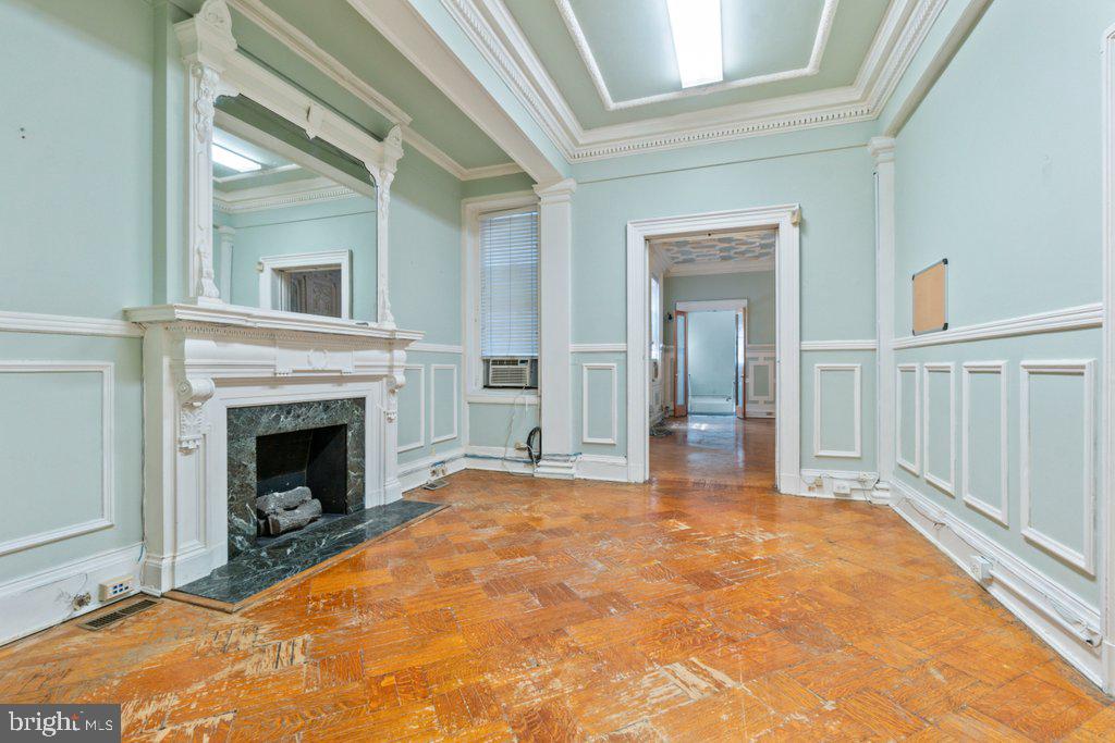 With ceilings soaring up to 13 feet and nearly 1,600 square feet of space, Unit 11 delivers the rare scale and grace of a Mount Vernon townhouse suite.
This refined, executive-level condominium offers five rooms—three of them private—providing flexibility for professional or residential adaptation. Two decorative mantels, parquet wood floors, detailed picture rail moldings, and intricate trim add to its formality and charm. A full bath serves the suite, and a private internal staircase connects Unit 11 to Unit 1 below. Together, Units 1 and 11 provide over 3,500 sq. ft. of contiguous space, combining the presence of a parlor-level suite with the practicality of a lower-level entry. Ownership will make Unit 11 self-contained if contiguous space is not desired. Tall windows fill each room with natural light, highlighting the craftsmanship and proportions that define Mount Vernon architecture.  The history: 
At the heart of Mount Vernon, 1118 and 1120 Saint Paul Street embody Baltimore’s architectural legacy. Designed and once occupied by George A. Frederick — the young prodigy behind Baltimore City Hall and the city’s park system — these brownstones reflect both history and craftsmanship. Now ,for sale within them are five distinct condominium units: dramatic parlor-level suites with soaring ceilings and ornate detail, alongside expansive lower-level spaces with flexible layouts and private entries. Together, they offer owner-users a rare mix of historic pedigree and practical adaptability in Baltimore’s cultural core.