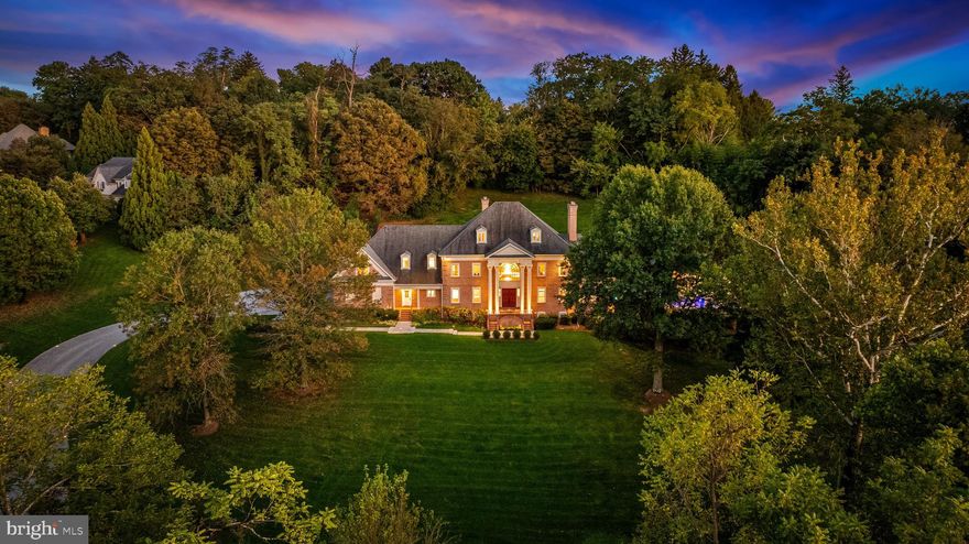 Tucked away on a serene 3.3-acre parcel in the heart of Ruxton, 1421 Wine Spring Lane is a distinguished Georgian estate where classic architecture meets modern sophistication. Thoughtfully reimagined by Mel Benhoff, this residence spans over 9,000 square feet and offers an exceptional blend of scale, craftsmanship, and privacy. A stately columned entrance opens to a dramatic granite foyer, setting the tone for interiors defined by symmetry, light, and timeless detail. Formal entertaining rooms are anchored by rich millwork and wood-burning fireplaces, while a sun-drenched family room and expansive chef’s kitchen invite everyday comfort. The upper level hosts a luxurious primary suite with soaring tray ceilings, a spa-inspired bath, and a bespoke dressing room. Additional bedrooms are generously proportioned, with elegant finishes and ample storage. A third-floor retreat and fully equipped lower-level gym provide flexible space for recreation and wellness. Outdoors, the grounds unfold into a private oasis with an infinity-edge pool, integrated spa, cascading waterfall, and fire features—all framed by mature trees and curated landscaping. A four-car climate-controlled garage, custom stained-glass accents, and whole-home smart systems complete the offering. Ideally positioned near Towson’s finest schools and amenities, this estate is a rare opportunity to live with grace, comfort, and enduring style.