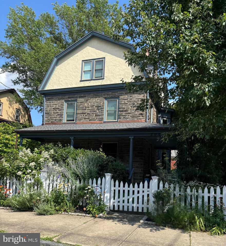 Tucked behind a charming white picket fence and lush landscaping, this beautiful 5 bed, 3
bath Wissahickon Schist Dutch Colonial home feels like something out of the Secret Garden.
A wraparound porch welcomes you home, inviting slow mornings with coffee and breezy
afternoons surrounded by the vibrant greenery.

Step inside to a warm and inviting entry foyer that leads to a light-filled living room, where
a gas fireplace sets the scene for cozy evenings. The dining room glows with natural light
from its elegant bay window, and the modern kitchen, with its soapstone countertops,
stainless steel appliances, and spacious island dares you to entertain. 

Beyond the kitchen, a versatile mudroom or den opens onto a patio overlooking the
enchanting garden. Mature fig, peach, and persimmon trees as well as year-round foliage including hydrangeas, roses, and lilies, create a private, leafy retreat that feels worlds away, even though you’re just ablock from Chestnut Hill’s shops, restaurants, and community events. The first floor also
features a combination full bathroom and laundry.

The sweet corner seat while you head upstairs is another reminder of the charm and
whimsy of this home. The second floor hosts three generous bedrooms, one with a reading
nook with a built-in bench, and all with ample closets. The large full bathroom off the
hallway has a tub that’s perfect for unwinding after a long day. The third floor is a serene
escape, featuring a primary suite with two closets and en suite bath, plus an additional
bedroom lined with a wall of closets.

Additional highlights include dual zoned high velocity forced air, radiator heat, and hardwood floors throughout,a full height, unfinished basement with tons of storage, a detached garage, and a private
driveway with room for three cars.

200 E Gravers Lane is a reminder that everyday can feel magical.