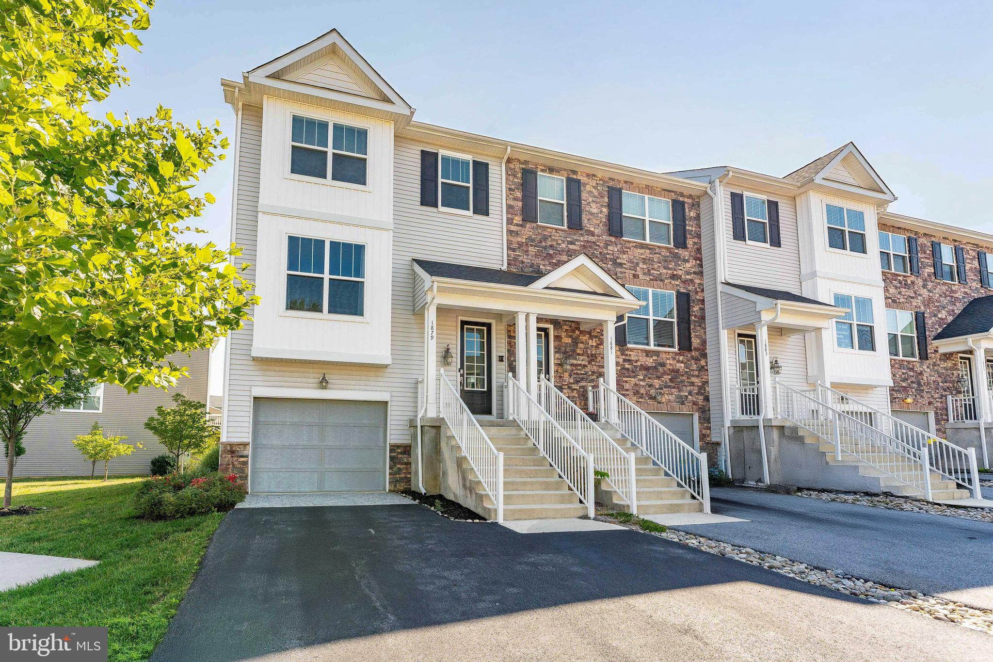 Welcome to 1879 Boulder Drive, a beautifully maintained end-unit townhome in the desirable Townes at Shannon Hill community of Downingtown. Built in 2019, this 3-bedroom, 2.5-bath Mayfair model offers a modern layout, stylish finishes, and low maintenance living. Upon entry, you're greeted by a spacious foyer featuring a partial two-story ceiling, elegant chandelier, powder room, Barringtown Hickory plank flooring, and a coat closet. Just a few steps up, the main level opens into a bright and inviting dining room with a double window and chandelier, seamlessly flowing into the living room and kitchen. The living room is filled with natural light thanks to a large double window, creating the perfect space to relax or entertain. The adjacent kitchen is both functional and stylish, featuring granite countertops, an island with seating, stainless steel GE appliances, white subway tile backsplash, and a convenient dry bar area with additional seating. Off the kitchen, the breakfast room offers a cozy spot for casual dining, complete with a chandelier and a sliding glass door that leads to the wood deck. This outdoor space overlooks a beautifully maintained courtyard and gazebo—an ideal setting to unwind and enjoy the view. Upstairs, the upper level includes a laundry closet, a linen closet, and three generously sized bedrooms. The primary suite boasts a tray ceiling, ceiling fan with light, plush carpeting, a walk-in closet, and a luxurious en-suite bathroom with tile floors, a double sink vanity, and a tiled shower with a glass door and bench seat. Down the hall, you’ll find a second full bathroom with tile flooring, a double sink vanity, and a tile tub/shower combo. Two additional bedrooms, both with carpet flooring—one featuring its own walk-in closet—offer flexibility for children, guests, or a home office. Back on the lower level, just a few steps down from the foyer, there's a cozy family room with access to the garage and a sliding door leading to the covered space beneath the deck. As a resident of Townes at Shannon Hill, you'll enjoy low-maintenance living with lawn care, snow removal, and landscaping included. The community also offers private access to a scenic walking trail, with permission granted by United Sports (USTC) to walk around the surrounding soccer fields. It’s conveniently located just minutes from local shopping, grocery stores, restaurants, and more. Don’t miss your chance to call this move-in-ready home yours!