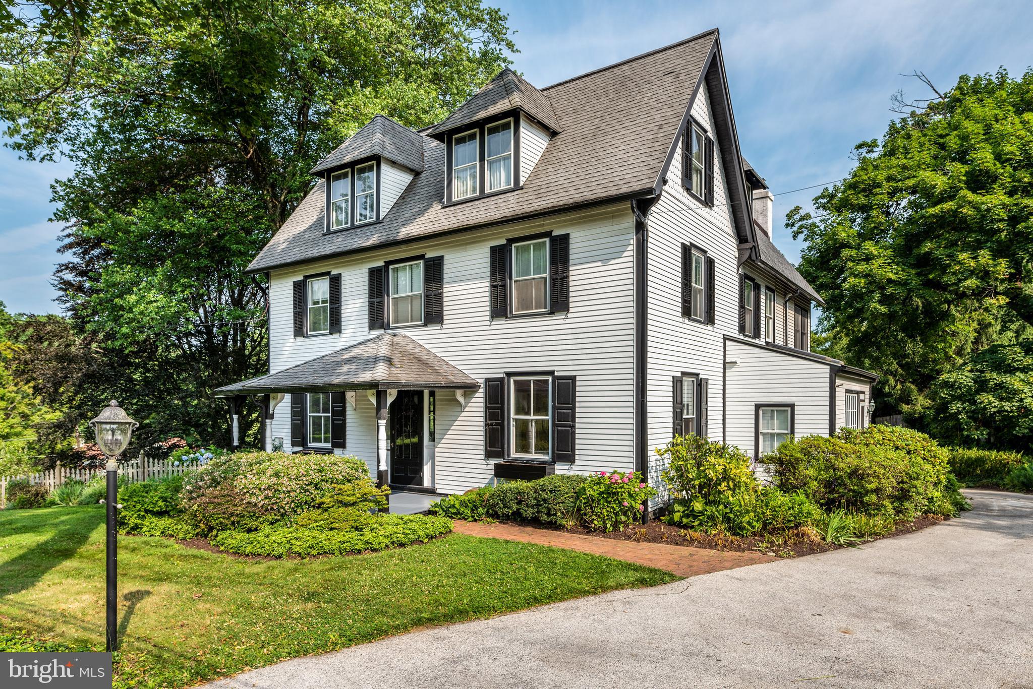 A true Penn Valley treasure in a bucolic setting! History lovers will delight at the timeless charm and enduring details of this fabulous 1880's 6BR, 3.5 BA Colonial Farmhouse on 3/4 acres of mature trees and plantings tucked away in a quiet, cherished Penn Valley location. From the covered front porch, one of multiple exterior spaces to enjoy, enter the center hall with chandelier and original red pine floors. To your left is the sitting/living room with an enchanting window that converts to a door to allow access to the covered side porch capturing summer's best breezes. The sitting room leads to the study/office with wonderful woodwork and the first of 3 wood-burning stoves. Opposite the sitting room is the dining room with plate rail, chandelier, red pine floors and swing-door access to the kitchen. The kitchen provides peninsula seating overlooking the family room, granite counter tops, lots of oak cabinet storage, a gas stove, new stainless-steel dishwasher, marble back splash, and access to the newer 1st floor powder room and laundry/mud room with convenient exit to the driveway. The family room addition has quaint built-ins, a Vermont casting stove, and opens to the screened-in back porch with ceiling fan and skylights, perfect for bug-free evening relaxation. Up the center stairs is the primary bedroom with recently-updated en suite bath, wood-burning stove and walk-in closet with organization systems. Three additional carpeted bedrooms and a charming hall bath complete this level. The 3rd floor offers 2 more good-sized bedrooms, a hall bath, an office, a bonus room, and storage. The detached 2-car garage has been converted to an art studio with vaulted ceiling, heat, water, concrete floors and triple barn doors, but could easily be transformed back to a garage that houses cars. The character and charm of this home continues in the back garden/patio area behind the garage, and includes a shed and a foot bridge that steps down to the lower lot. With easy access to Philadelphia, award-winning Lower Merion schools, and all major highways, this home offers a nod to yesteryear with all the conveniences of modern living.