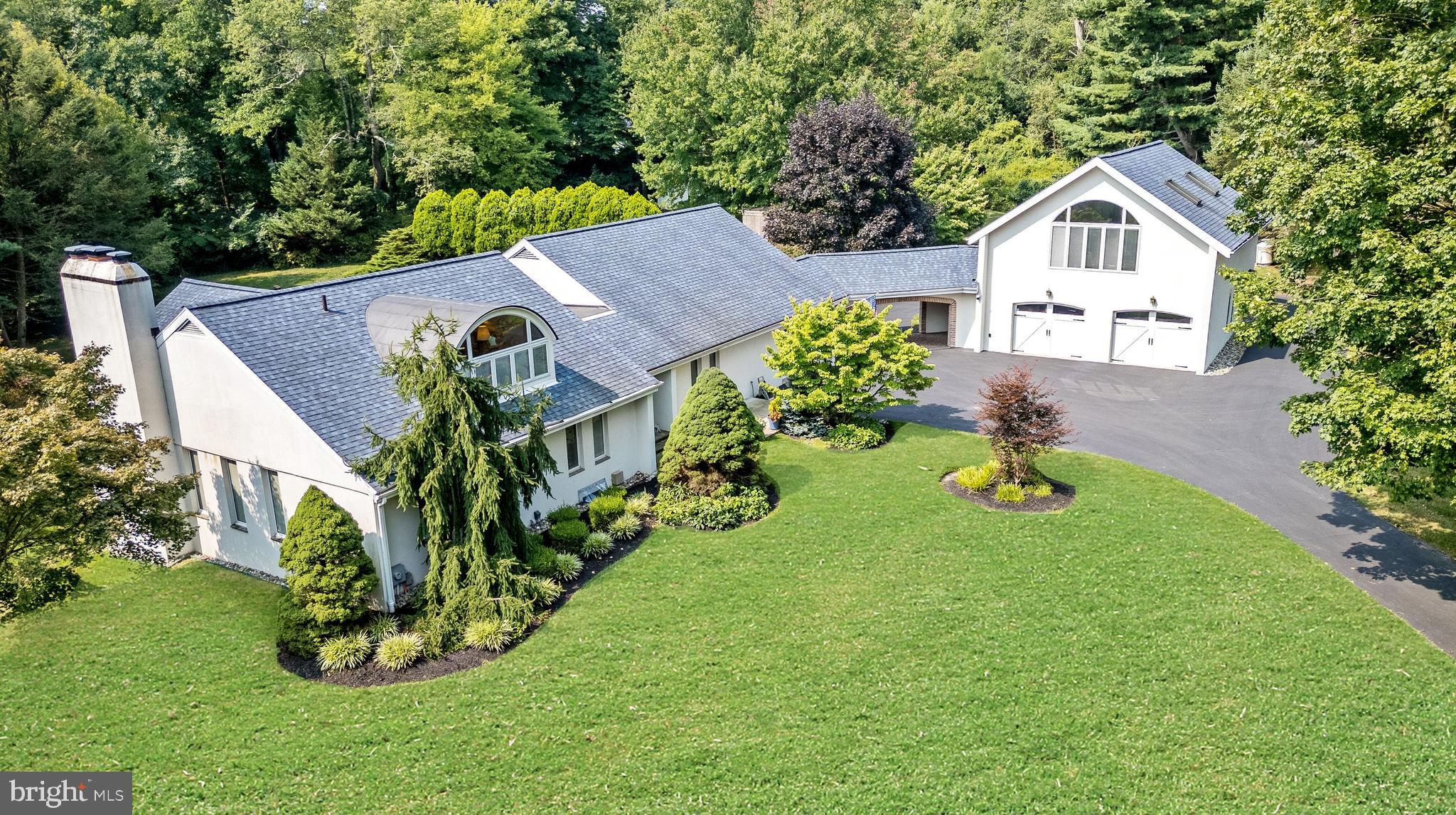 LOWER TAXES!! Located in a secluded enclave off a private drive in desirable Whitpain Township, this custom architectural-style home is set on beautifully manicured grounds with mature trees, lush gardens, and expansive open space. As you enter into the foyer, you're welcomed by warm hardwood flooring that flows through much of the main level, setting the tone for the elegance found throughout the home. The spacious and sun-filled living room features oversized windows and a sliding glass door that leads to a serene rear patio, where a charming paver walkway guides you to the inviting in-ground pool and landscaped backyard — perfect for entertaining or peaceful relaxation. The eat-in kitchen offers gorgeous cabinetry, granite countertops, a stylish tile backsplash, stainless steel appliances, and durable tile flooring. Just off the kitchen is a large pantry, and a mudroom with convenient access to the garage and rear yard. The formal dining room is equally impressive, anchored by a beautiful wood-burning fireplace flanked by windows and accented by views of the staircase that leads to the second floor. The main-level primary bedroom offers a spacious walk-in closet featuring custom built-ins and an elegant en-suite bath complete with tiled floors, a separate washroom and water closet, and a stunning walk-in shower enclosed by seamless glass. Two additional bedrooms on this floor offer ample closet space and share a well-appointed full bathroom with tile flooring, a dedicated washroom, and a water closet with a sunken tub and seamless glass shower enclosure. Upstairs, a fourth bedroom offers extra privacy and comfort with a walk-in closet and a stylish full bath featuring a tiled walk-in shower with seamless glass. The finished lower level adds additional living space with a cozy family room complete with a wood-burning stove and tile floors, plus a separate utility room that houses the laundry and mechanical systems, and space for storage.
A unique highlight of this home is the separate in-law suite located above the separate two car garage that is connected by a covered breezeway, offering efficiency-style living with hardwood floors, two full closets, a wet bar, and an updated full bath with a walk-in tile shower and tasteful fixtures making it ideal for extended family and guests. The exterior of the home is equally impressive with its well-maintained landscape, mature plantings, in-ground pool, and open green space perfect for recreation or relaxation. This home seamlessly blends thoughtful design, comfort, and elegance in a truly tranquil setting. The This home was been well maintained and tastefully updated throughout ownership. Pella windows throughout, roof recently replaced. Home owners association maintains the private entry road which includes plowing and common area landscape.