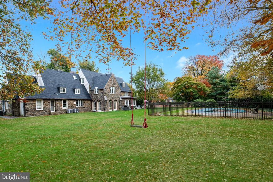 This enchanting storybook English manor home will capture your heart with its gorgeous stone exterior, stunning architectural detail, and sprawling lush grounds with an in-ground pool. Grace and elegance await in the finely renovated, classic yet contemporary interior. An entryway with coat closet and foyer with powder room are encountered upon arrival, introducing impeccable living quarters accented by a striking winding staircase, lovely crown and chair rail moldings, 3 fireplaces, and rich hardwood floors throughout. Comfortable living and formal entertaining are all well accommodated in the spacious main public rooms. A large family room punctuated by a gas-burning fireplace and large bay window opens to a library with walls of tasteful built-ins. French doors access the beautiful rear patio with generous seating and dining areas, and stretching lawn and pool beyond. Share formal meals with family and guests in the warm, sophisticated dining room with a gas fireplace, crown moldings, and 2 built-in china cabinets flanking large windows. The well-equipped chef s kitchen, beautifully updated in 2012, is appointed with marble countertops, abundant cabinetry, a large island with 2nd sink and storage, and huge pantry. Top-grade stainless steel appliances include 2 Bosch dishwashers, Subzero fridge, Dacor oven and a wine fridge. Enjoy casual fare in the breakfast area, or step out with a coffee or cocktail to the lovely sunroom featuring stone flooring, and doors leading out to the patio. Connected to the attached 2-car garage and driveway is a convenient mudroom with slate floors, a mini fridge, cubbies and coat closet. Perched on the 2nd floor are 4 bedrooms and 5 baths, plus a bonus space or bedroom. The peaceful master boasts large walk-in closets and a private bath with dual sinks, steam shower, and plumbing for a tub. There are 2 additional en-suites, a hall bath, laundry room with storage, and nanny/in-law suite positioned by the rear staircase. Level 3 offers 2 more bedrooms with vaulted ceilings, a Jack-and-Jill bath, big cedar closet and excellent storage. Topping the allure is the prime Lower Merion Township location near top-rated schools, Suburban Square, shopping, dining and recreation, the train and major routes.