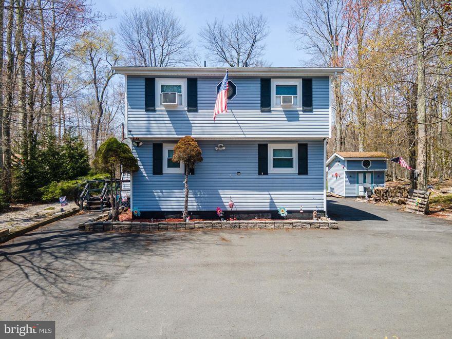 Tucked away in the scenic Pocono Mountains, this charming 2-bedroom, 2-bath contemporary home with a full vinyl facade offers comfort, character, and privacy. A large wraparound paved driveway begins at the front and extends around three sides of the home, providing ample parking for guests. Inside, wall-to-wall carpet flows throughout the open-concept family and dining rooms, highlighted by a vaulted ceiling with skylights and a ceiling fan. The family room features striking floor-to-ceiling wood-paneled walls and a stone fireplace with mantel, creating a warm and inviting atmosphere. The bright dining area includes sliding door access to a walkout deck—perfect for relaxing during long summer evenings surrounded by lush trees. The open kitchen is equipped with stainless steel appliances and sink, recessed lighting, a ceiling fan, and a convenient breakfast peninsula. The first-floor bedroom offers wall-to-wall carpet and easy access to a full bath with luxury vinyl plank flooring and a tub/shower combo. Upstairs, a finished loft provides a versatile space ideal for an office or sitting area with views overlooking the family room. An additional bedroom with a vaulted ceiling, wall-to-wall carpet, and dual closets, along with a full bath featuring luxury vinyl plank floors, tub/shower combo, and linen closet, completes this inviting home. Conveniently located close to major highways I-80, I-380 and I-84 for easy commute, Camelback Ski Resort, K Pool, Dresser Lake Park, Pocono Farms Country Club Association, shops, restaurants and so much more! *ALL FURNITURE & BELONGINGS INCLUDED IN THE SALE*