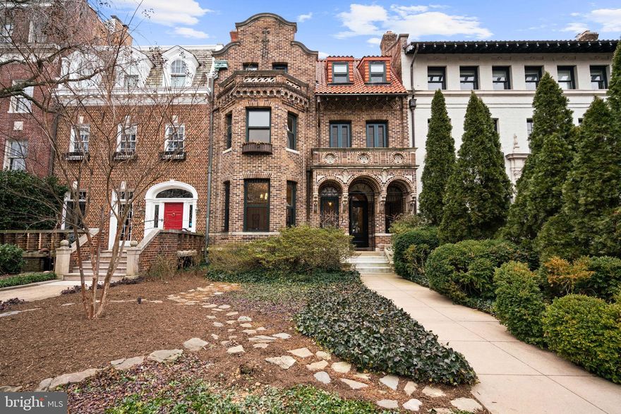 Built in 1910 and designed by prominent Washington architect Waddy Butler Wood, 2214 Wyoming Avenue is one of three attached, speculatively-built residences that together form one of the most sophisticated row house compositions in the city. A distinguished example of Wood’s Arts & Crafts interpretation of Mediterranean Revival architecture, the home’s richly ornamented façade is crafted of concrete by the renowned John Early Studio, the same artisans responsible for the historic walls at Meridian Hill Park. Set among a remarkable collection of ambassadorial homes, the residence is one of more than five dozen properties in Kalorama designed by Wood. 
Behind its whimsical exterior, the interior spaces offer a seamless flow designed for both grand entertaining and comfortable everyday living. The main rooms transition effortlessly from one to the next, creating an inviting progression through the home and a natural setting for gatherings of any scale. Architectural detail and craftsmanship are evident throughout, providing a backdrop that reflects both history and individuality. 
The residence is set back from the street and approached through a garden. From a covered front porch, the home opens into a gracious foyer where classical detailing and elegant crown moldings establish the tone of the refined interiors. The home balances multiple periods and styles with confidence. Neo-classical detailing defines the foyer and living room, which features a fireplace, built-in bookcases, and expansive bay windows that fill the space with natural light. The adjoining dining room offers a striking contrast, evoking the medieval period with wood-paneled walls, a gothic-arched fireplace, and leaded-glass doors. The interiors flow into a kitchen appointed with a suite of stainless-steel appliances, a butler’s pantry, wine cellar, and an adjoining breakfast room, which opens to the rear terrace and a three-car garage, creating an effortless connection between indoor and outdoor living. A powder room completes the main level.
Upstairs, the primary suite at the front of the house provides a serene retreat, with a walk-in closet, sitting room, and bathroom suite. A generous bedroom at the rear, warmed by a fireplace, offers views of the garden, and a paneled office shares access to a well-appointed hall bathroom. A skylight illuminates the staircase leading to the third floor, which features a generously sized bedroom with an adjoining sitting room, a private balcony overlooking the picturesque street, and an ensuite bathroom. Two additional bedrooms share a full hall bathroom, completing this level with ample space for residents and guests.
The expansive lower level with high ceilings offers abundant room for storage and future expansion, already equipped with a powder room, a full bathroom, and exterior staircase. This versatile space provides a blank canvas for a recreation room, home office, or guest suite, enhancing the home’s flexibility. 
Ideally situated on one of Kalorama’s most admired streets, 2214 Wyoming Avenue is surrounded by Washington’s most historically and architecturally significant homes and has long been associated with presidents, diplomats, and dignitaries. Centrally located and within walking distance to Mitchell Park, neighborhood coffee shops, Georgetown, Rock Creek Park, and the Dupont or Woodley Metro stops, this distinguished residence represents a rare opportunity to own a truly important home in one of the District’s most storied and enduring neighborhoods.