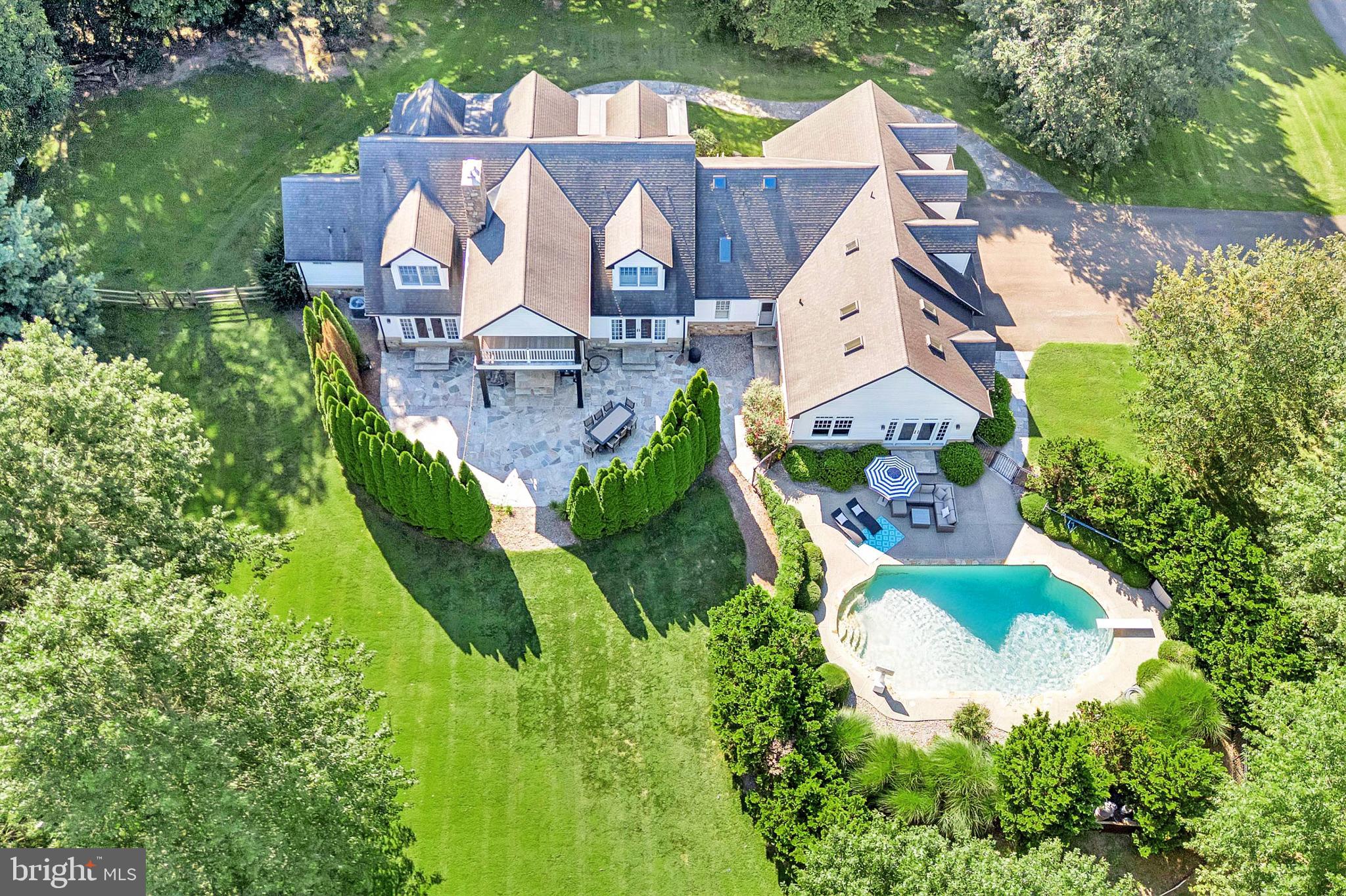 This one-of-a-kind executive estate blends timeless Cape Cod architecture with modern sophistication, set high on over 10 rolling acres to capture the very best of Chester County living. A sweeping covered flagstone porch (10x50) welcomes you into a grand foyer, where custom-milled hardwood floors, crown molding, nine-foot ceilings, and rich stonework set the tone for the exceptional quality throughout. Built without compromise, this home was designed for one-level living and is wheelchair-accessible on the main level, highlighted by a luxurious owner’s suite with a spa-inspired bath featuring a state-of-the-art walk-in shower, dual custom vanities with marble tops, and a custom walk-in closet with organizer. The chef’s kitchen is an entertainer’s dream, featuring granite countertops, extensive cabinetry, an oversized island with prep sink, a Thermador six-burner gas range with double ovens, SubZero refrigerator, Miele drawer dishwasher, trash compactor, and built-in pull-out pantry, all flowing seamlessly into both formal and casual dining spaces with French doors opening to outdoor living. The living room impresses with a gorgeous stone fireplace with wood stove insert, custom built-ins, window seats, and arched doorways, while a breathtaking library with custom-built, floor-to-ceiling wood shelving and French doors to the covered stone porch offers warmth and refinement. Completing the main level are a spacious guest bath designed for poolside convenience, a commercial-grade sauna, and a radiant-heated floors! Huge mudroom/laundry with abundant storage. Upstairs, you’ll find four generously sized bedrooms (one en suite), a hall bath, a media lounge with a 10-foot drop-down screen and projector, and a huge private au pair/guest suite with wet bar that opens to a versatile bonus room with surround sound and balcony views. Additional highlights include an oversized three-car garage with 8-foot wooden doors, a tiled game and entertainment room with French doors to the pool, two newer HVAC systems, surround sound throughout the main floor, a whole-house water treatment system, and countless custom touches. Outdoors, the property lives like a private resort with a sparkling swimming pool, multiple flagstone terraces, lush lawns, and more than five wooded acres with walking trails. Nestled among Amish farms and horse country, this remarkable estate offers a rare opportunity to experience refined living, natural beauty, and everyday tranquility.
