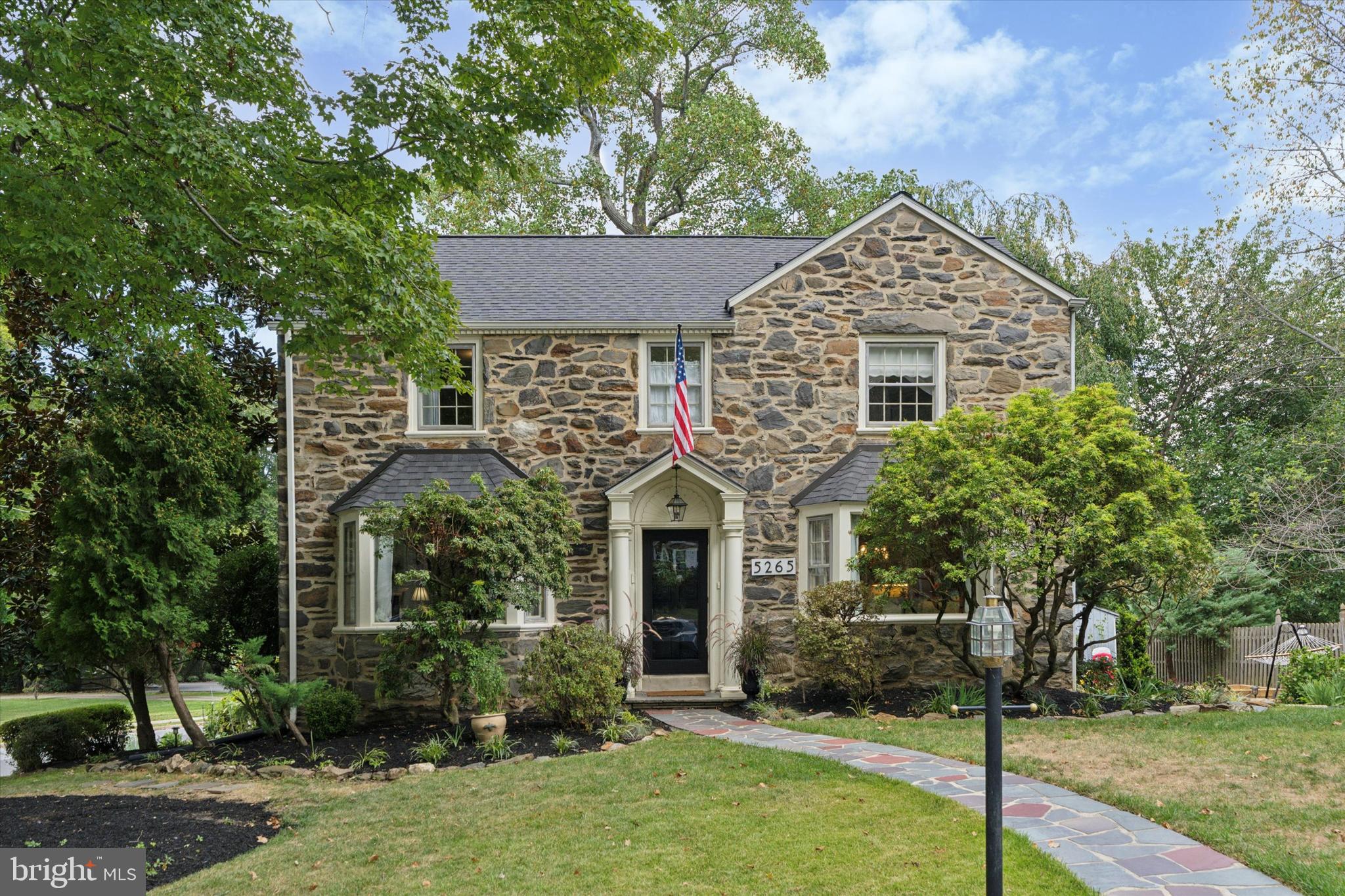 Welcome to 5265 Apache Lane. Tucked away in a coveted neighborhood, warmth & charm fill this 4-bedroom, 2-full bathroom, 2-half bathroom, single home in Pilgrim Gardens. This traditional stone colonial with picturesque curb appeal and greenery is situated on a large corner lot. A welcoming center hall entrance foyer anchors the spacious living room with the formal dining room. Adding elegance are the hardwood floors, stone gas fireplace, and bay windows. A dazzling updated kitchen with stainless steel appliances and granite countertops leads to the sundrenched breakfast room and family-room addition. Drift outside for coffee on the deck or have a catch in the yard; the outdoor space is ideal. A powder room and large closet complete the main floor. On the second floor you will find the grand main bedroom addition with vaulted ceilings, multiple closets and an ensuite bath, and three more bedrooms and an updated full bathroom. With over 2,500 square feet of main living space, this spectacular home is further enhanced by an additional 500+ square foot finished walkout basement, complete with a half bath. Don't miss the brand new roof that was installed in August (2025). A swift walk to Aronimink Swim Club, a quick drive into the city, easy access to public transportation, and great for walking to restaurants and shops. Welcome home.